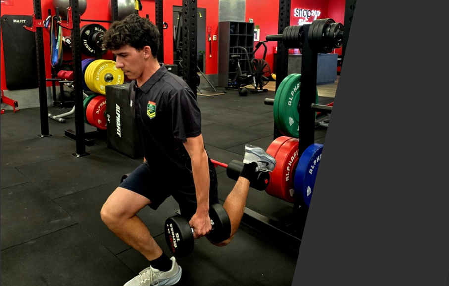 Young man performing a Bulgarian split squat with a dumbbell in a gym.
