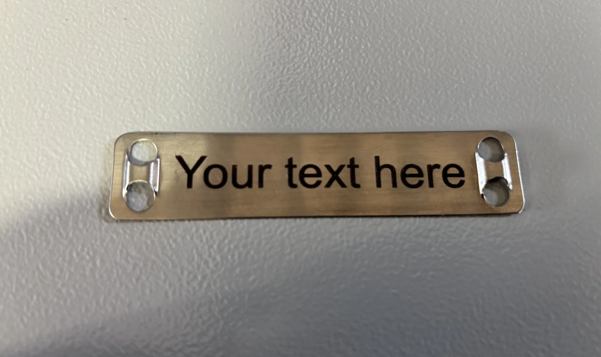 Stainless steel cable marker installed on electrical cable, showing engraved text