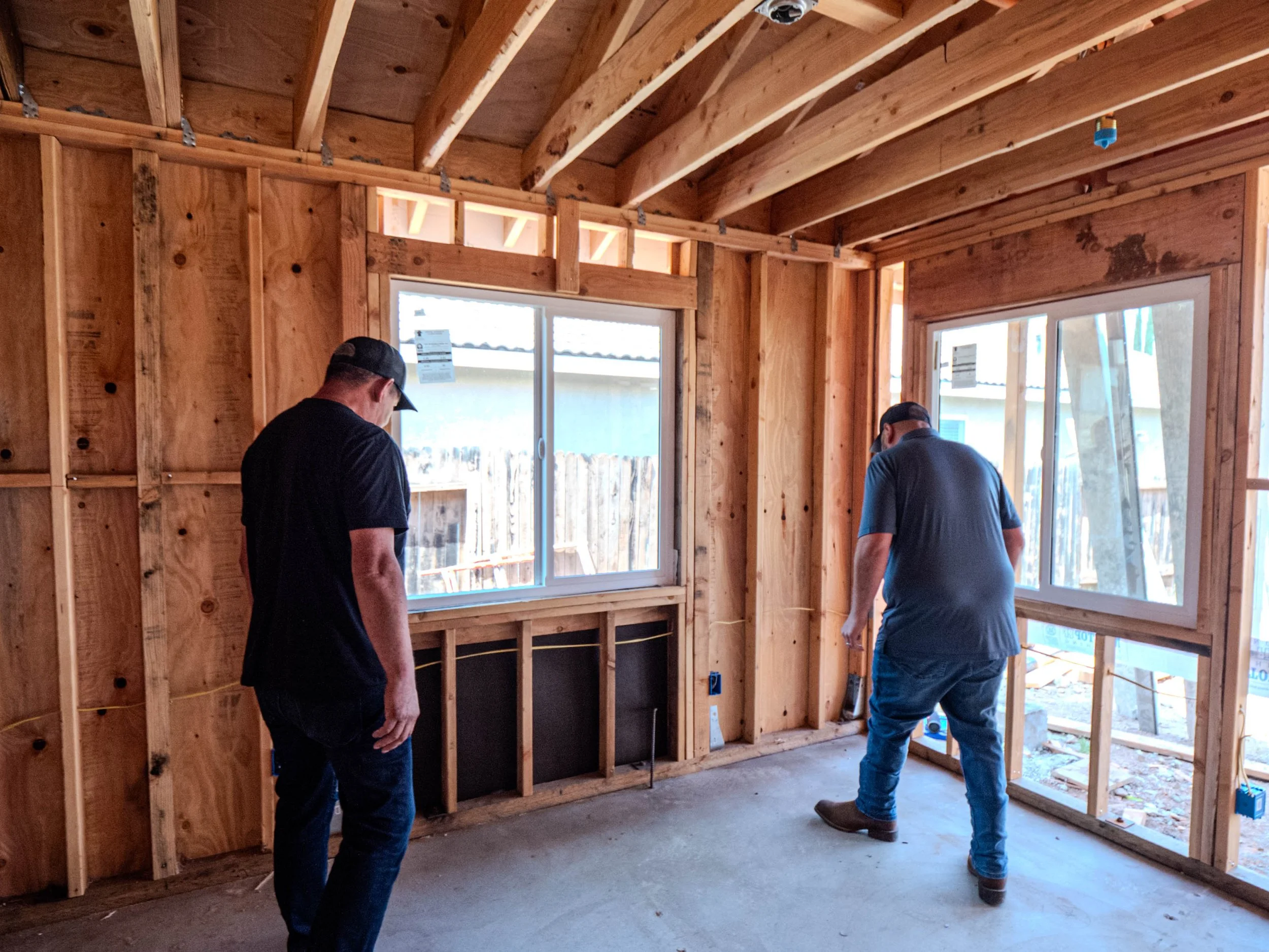 Two men inspecting framing inside a new construction building with wooden studs and roof trusses.
