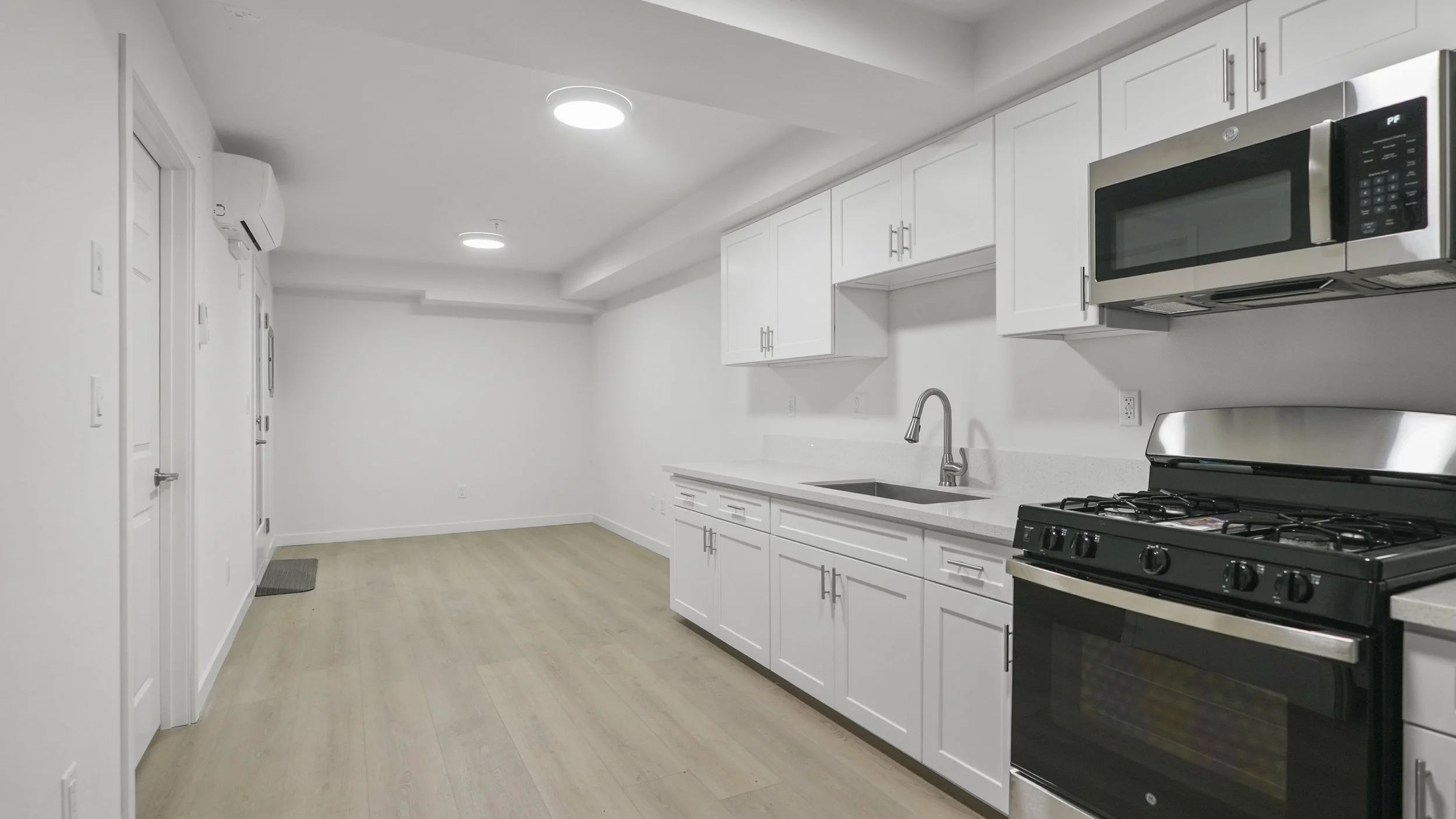 Modern kitchen with white cabinets, stainless steel microwave, black stove, and light wood flooring, illuminated by ceiling lights.