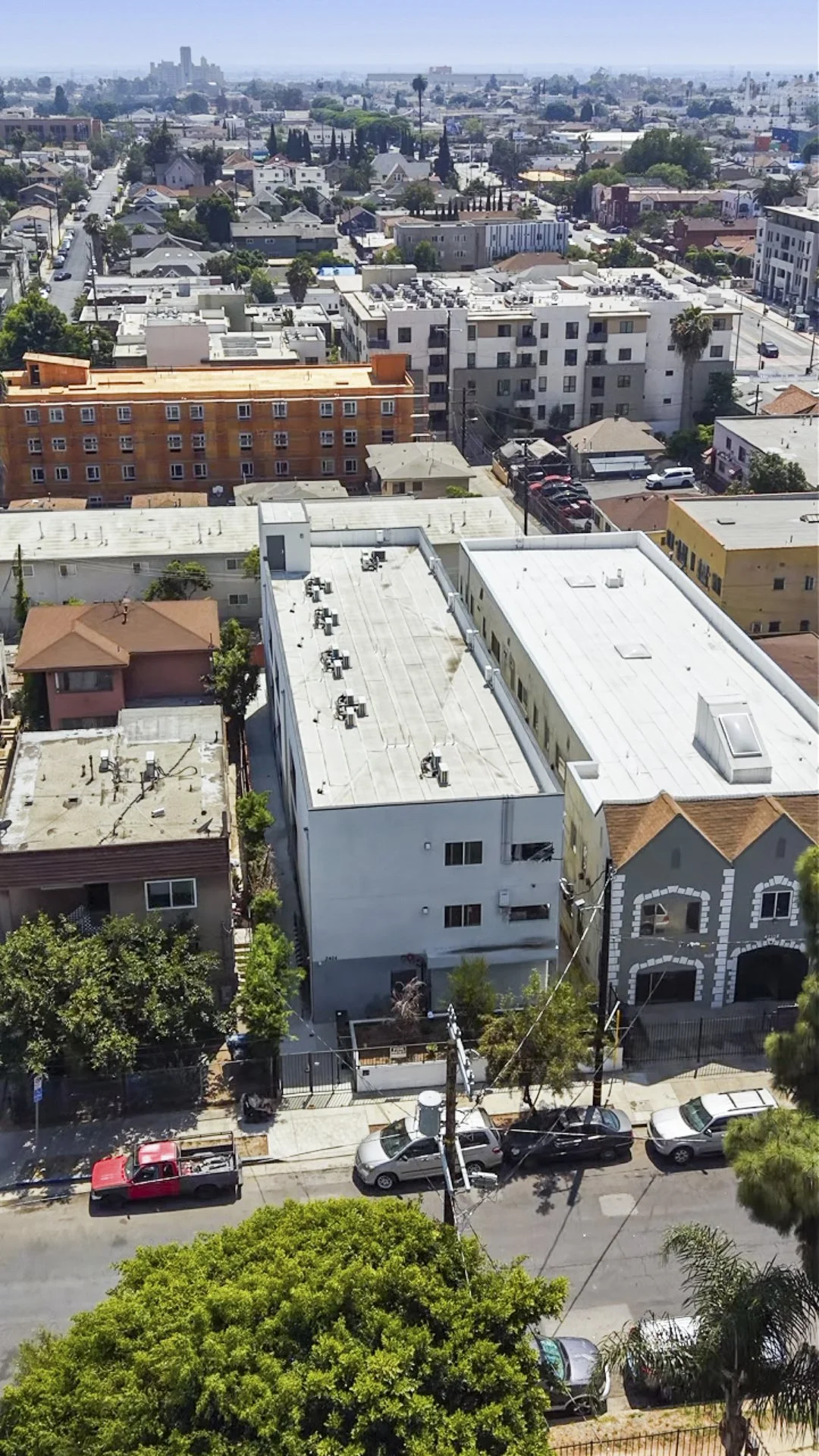 A cityscape view of rooftops, streets, and buildings in an urban area, with trees and parked cars in the foreground.