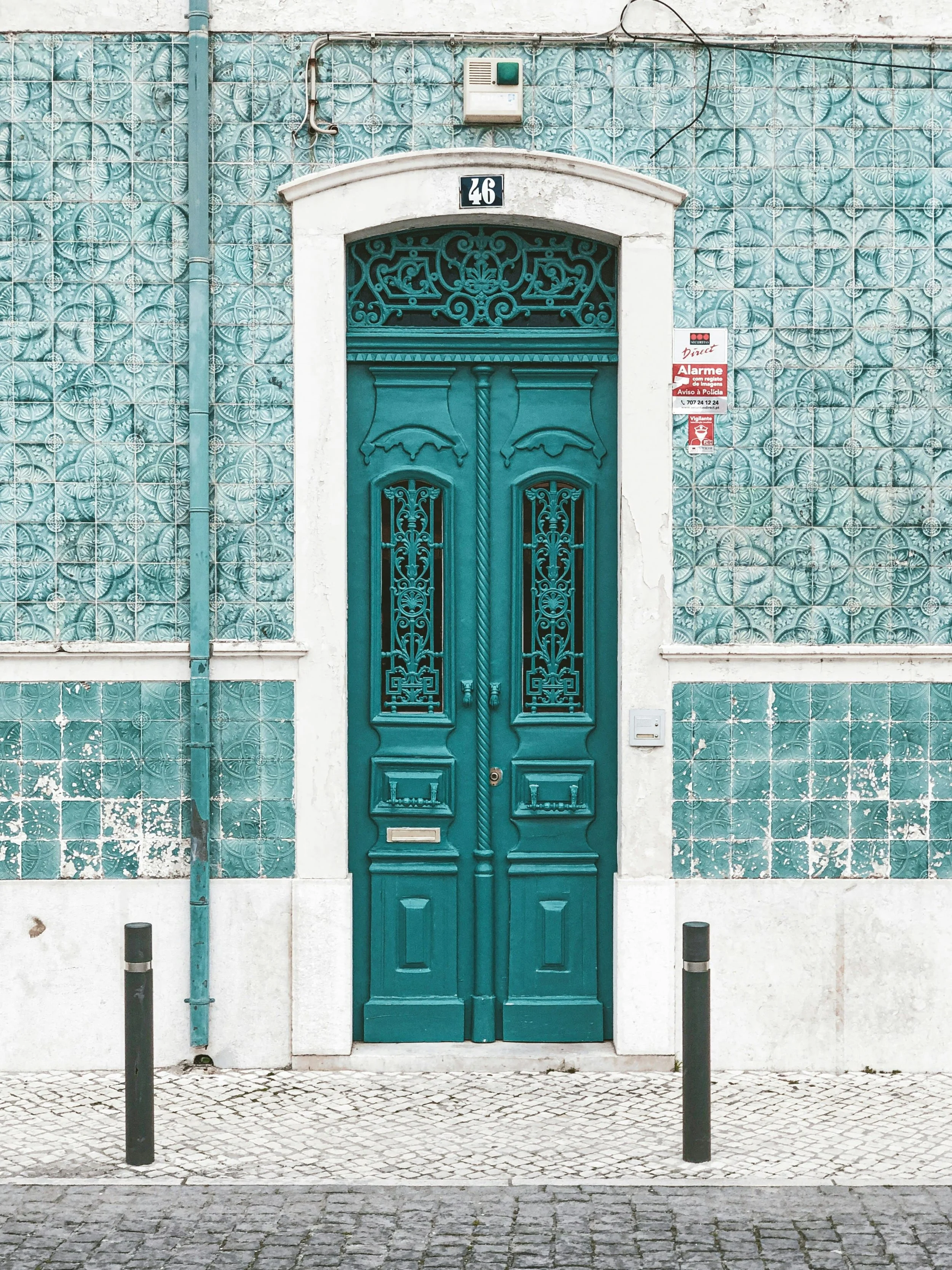Decorative teal double door with ornate ironwork, white stone trim and surrounded by patterned teal tile wall, in an urban setting.