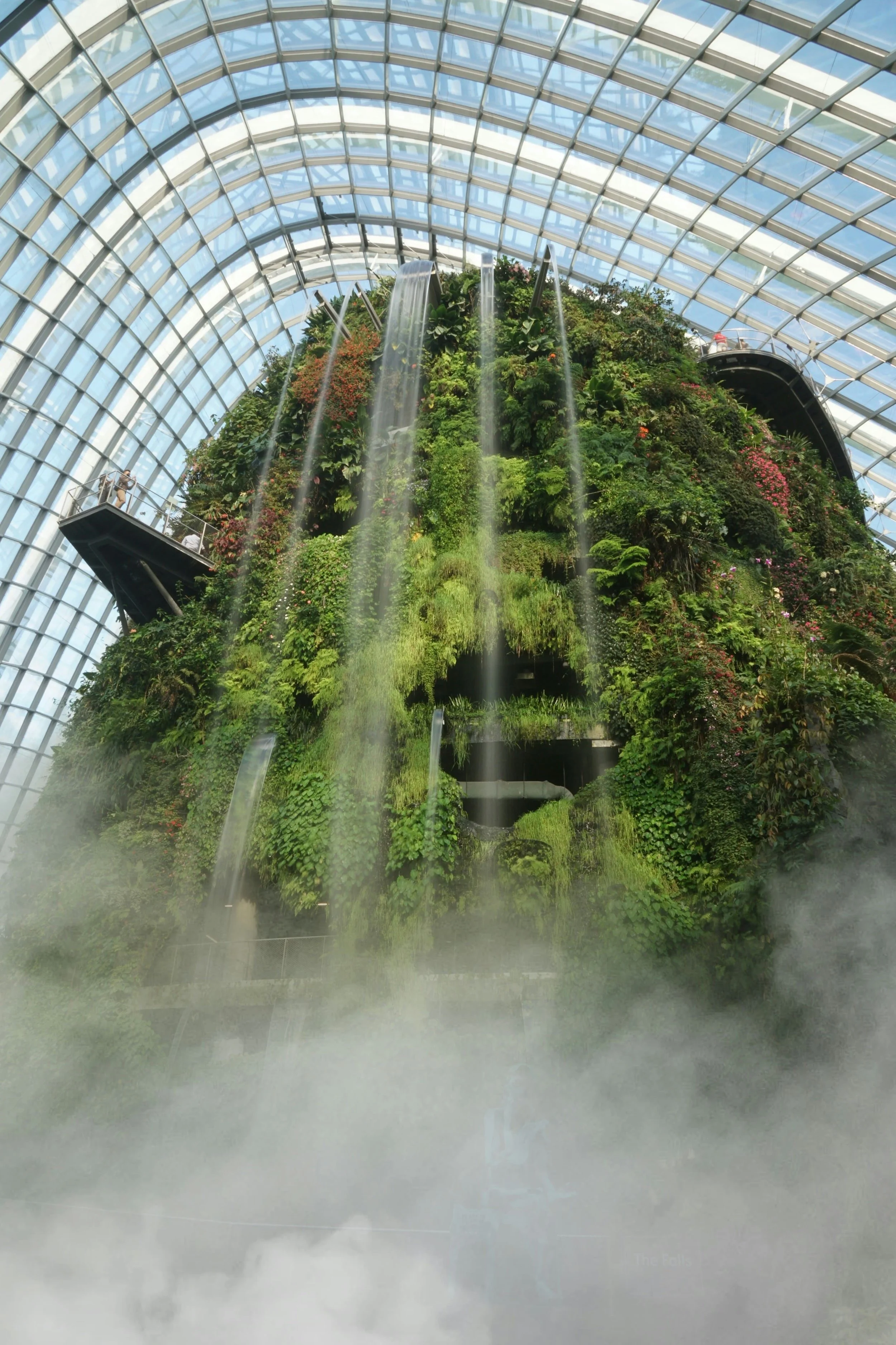 Indoor waterfall with lush greenery inside a glass-domed conservatory