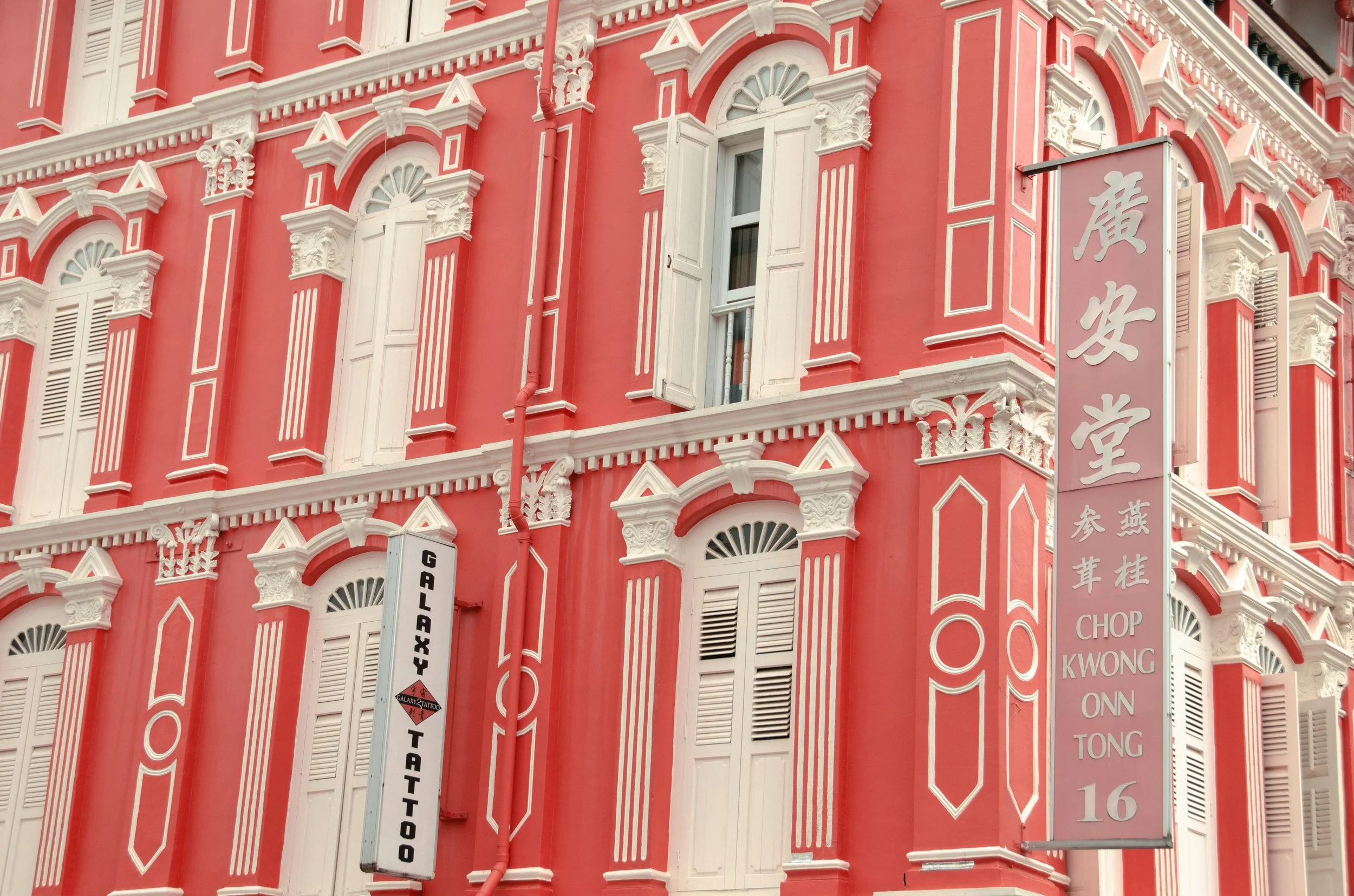 Pink historical building with white decorative trim, windows with shutters, and vertical signs with Chinese characters, including one for "Galaxy Tattoo".