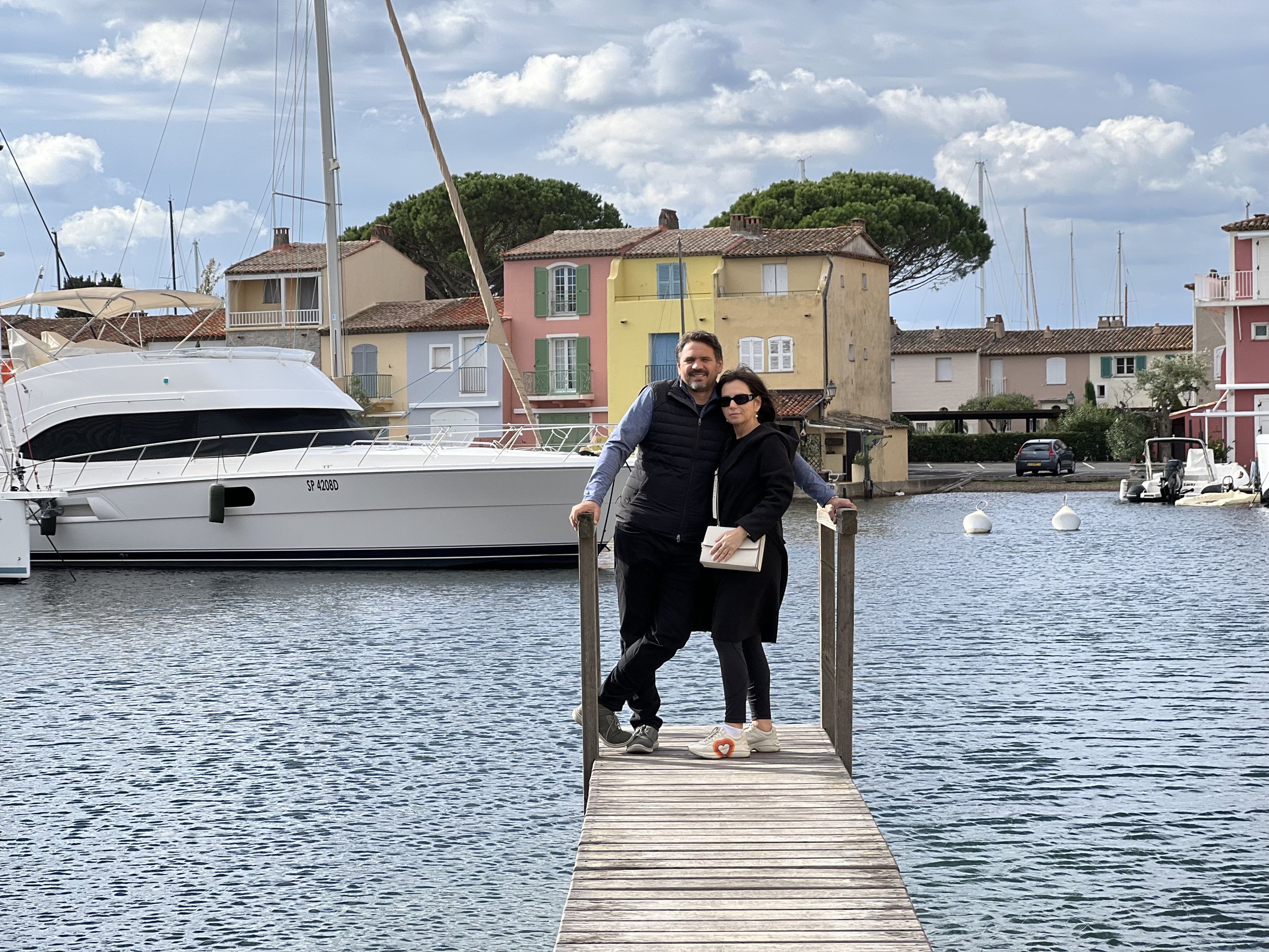 Couple standing on a dock with a boat and scenic waterfront view in the background.