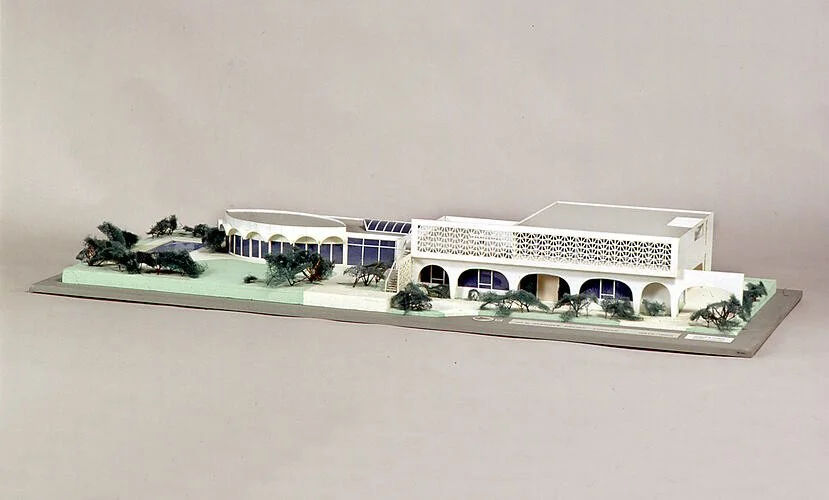 A detailed architectural scale model of a modern building with trees around it, featuring curved and rectangular sections, and a patterned facade.
