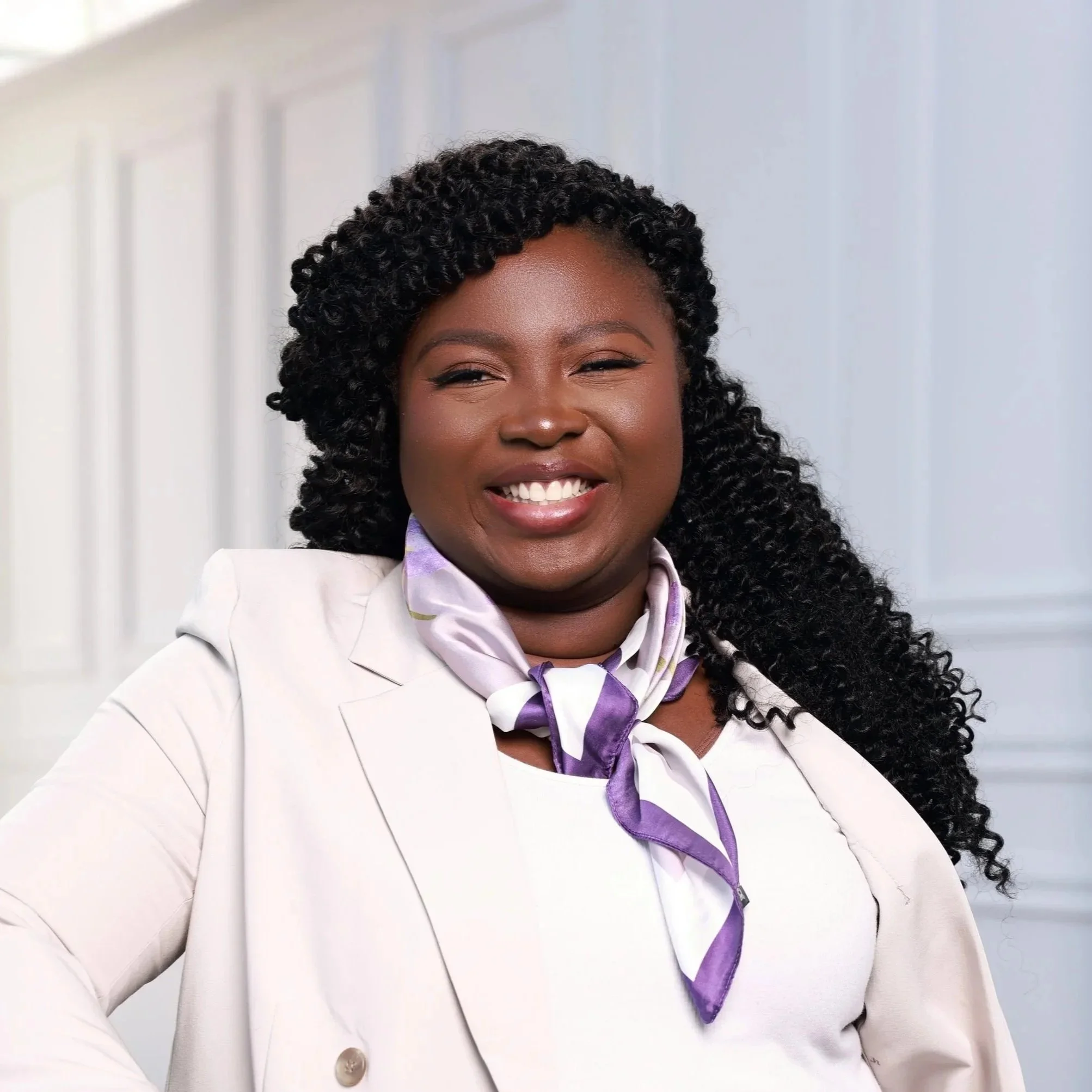 Smiling person sitting on a chair with a laptop in their lap, wearing a black and patterned dress against a dark background.