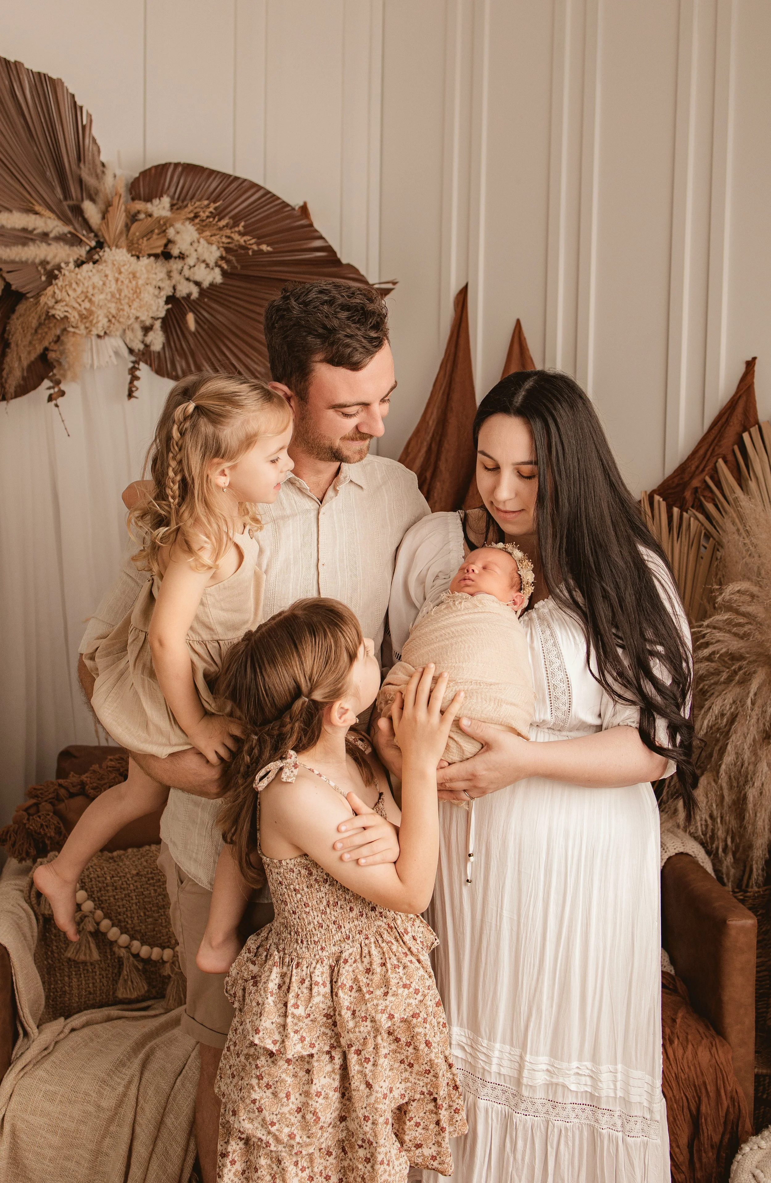 Family of five celebrating a newborn baby, with two young girls and a father gathered around mother holding the baby in a cozy, decorated room.