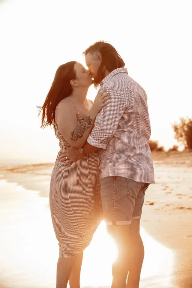 A couple standing close on a beach during sunset, about to kiss.