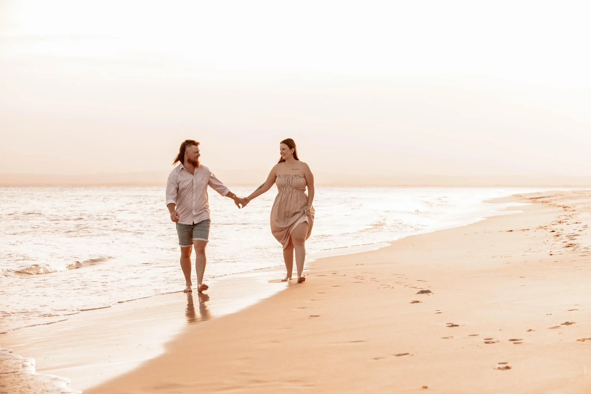 A couple walking hand in hand along the beach at sunset, leaving footprints in the sand.