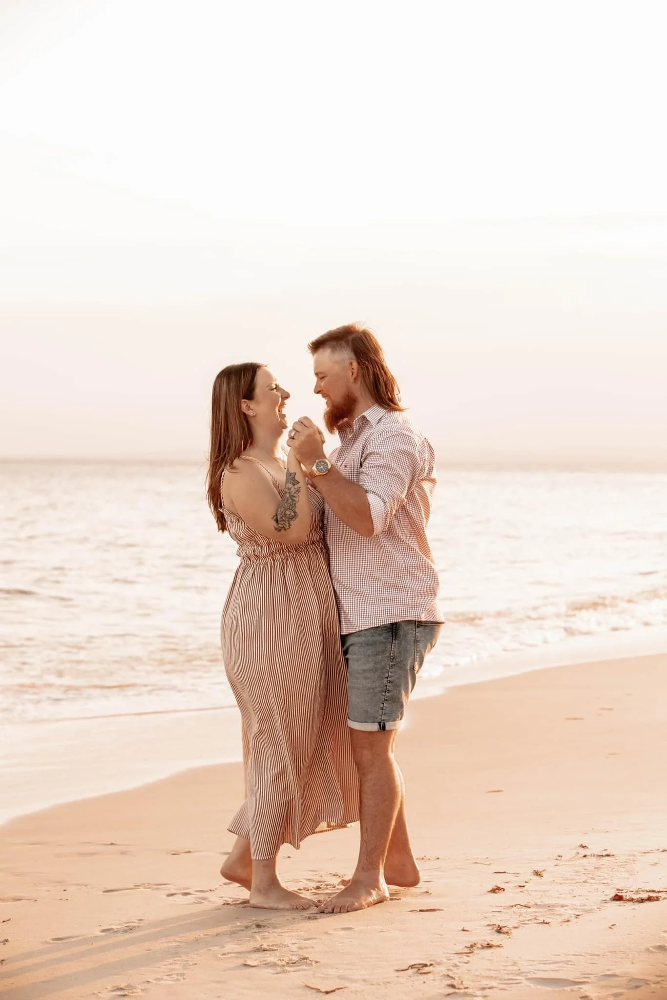 A couple dancing and smiling on the beach at sunset.