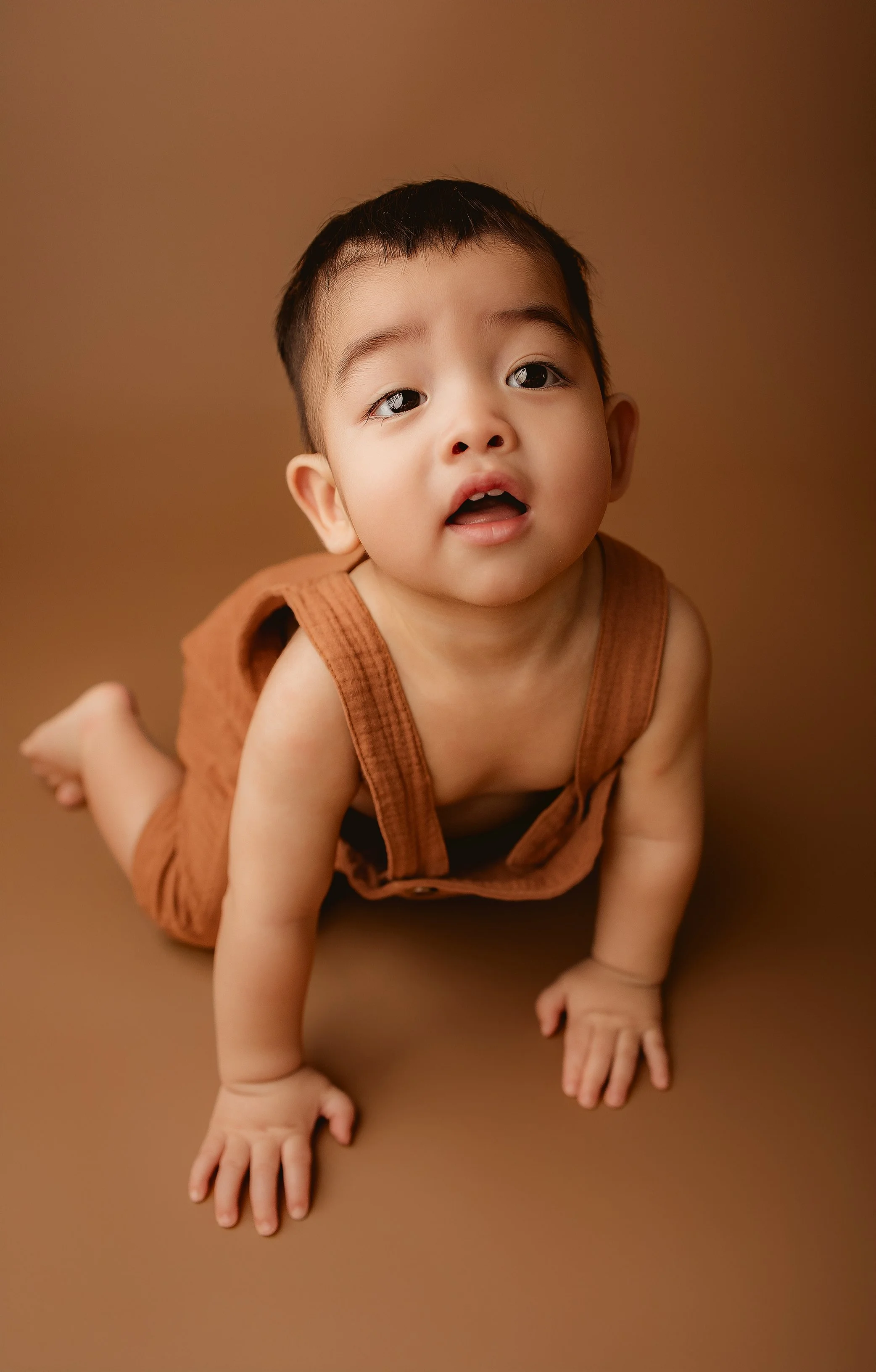 Young child crawling on a brown surface, looking up with a curious expression.