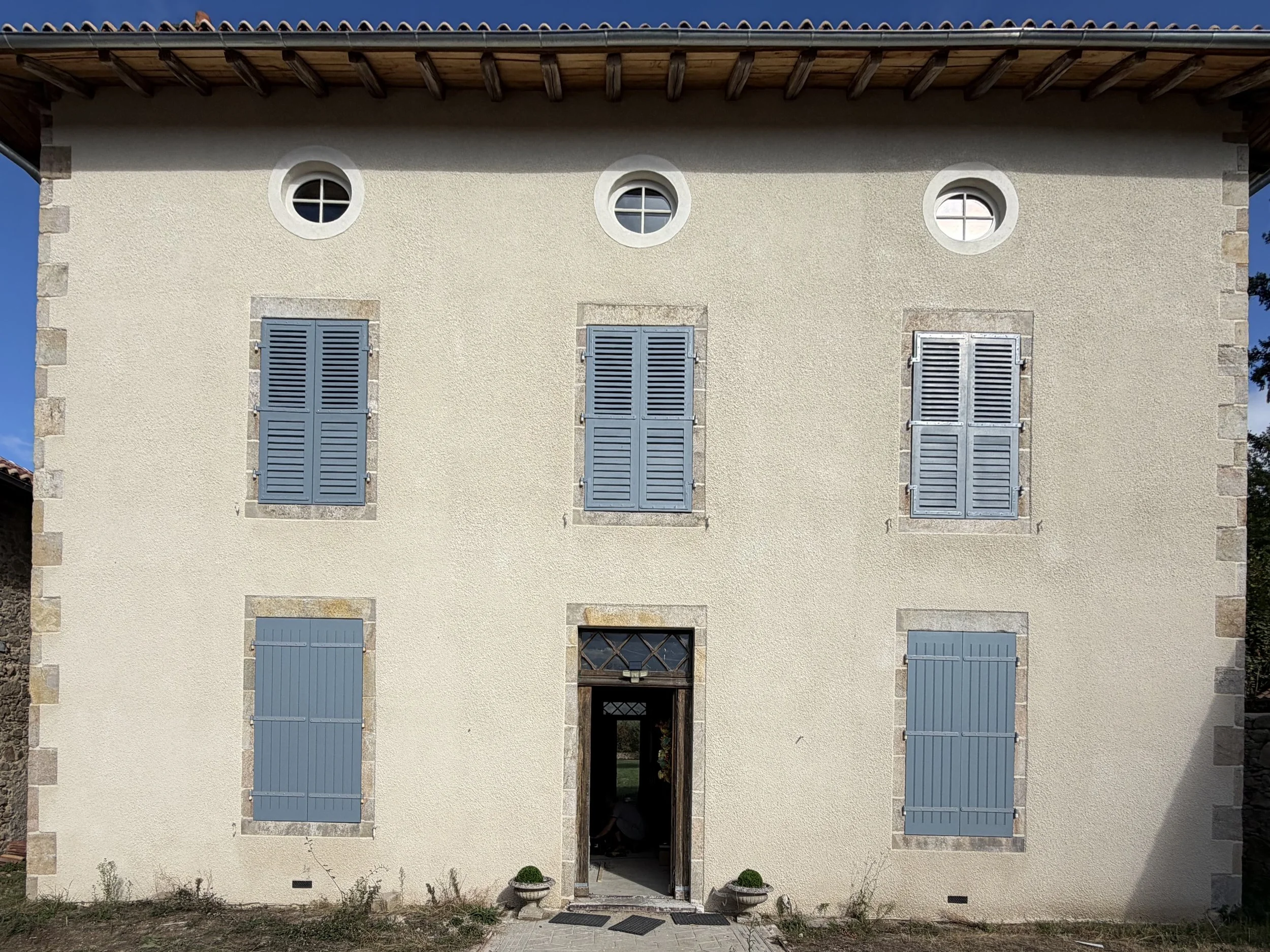 Les Cars (87) — l'ensemble des menuiseries de la façade : volets persiennés à l'étage, volets pleins au rez-de-chaussée, et trois œils-de-bœuf. Tout a été fabriqué à l'atelier de Brie pour les ouvertures existantes.