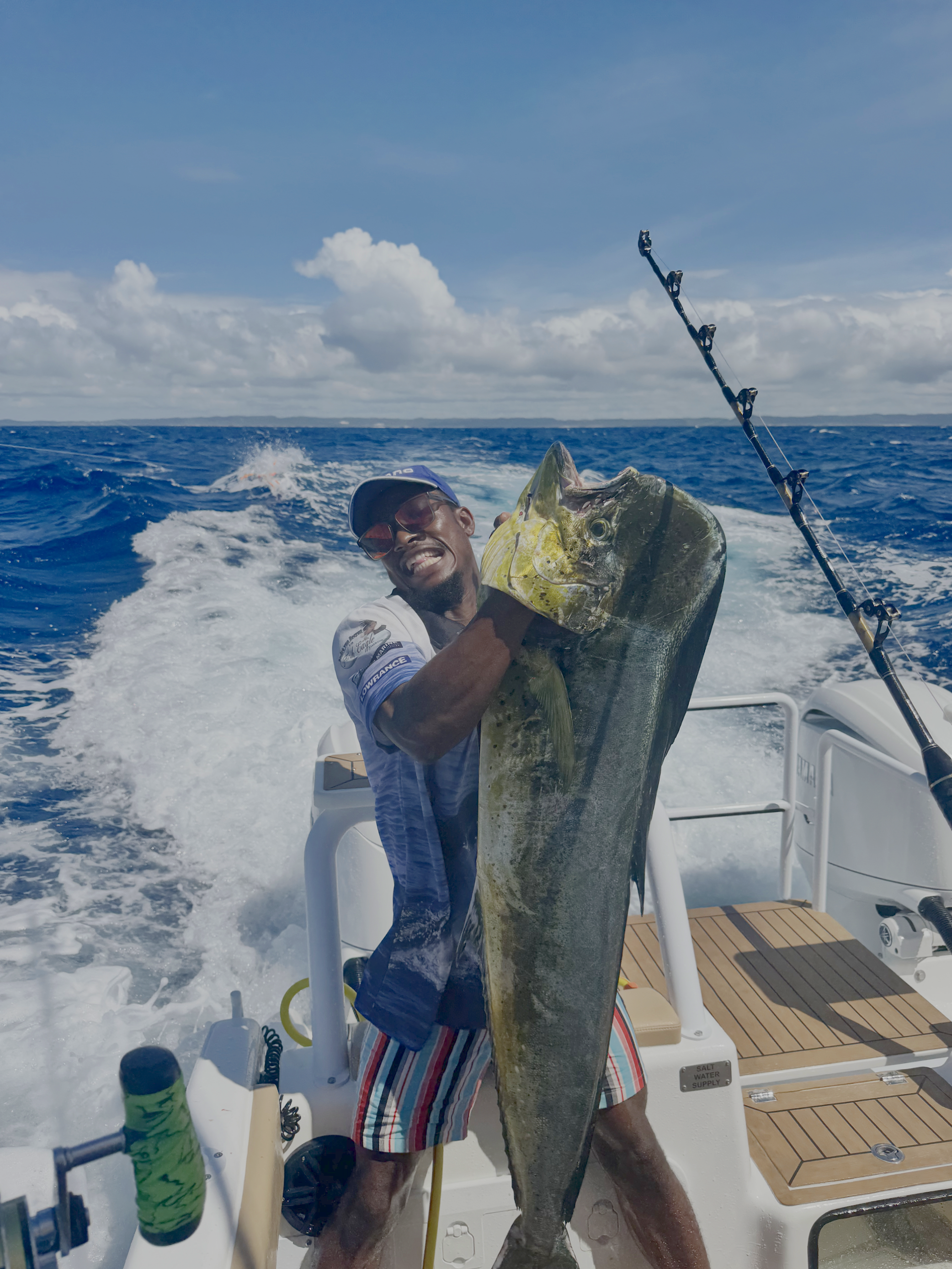 A man on a boat holding a large fish with an ocean and cloudy sky in the background.