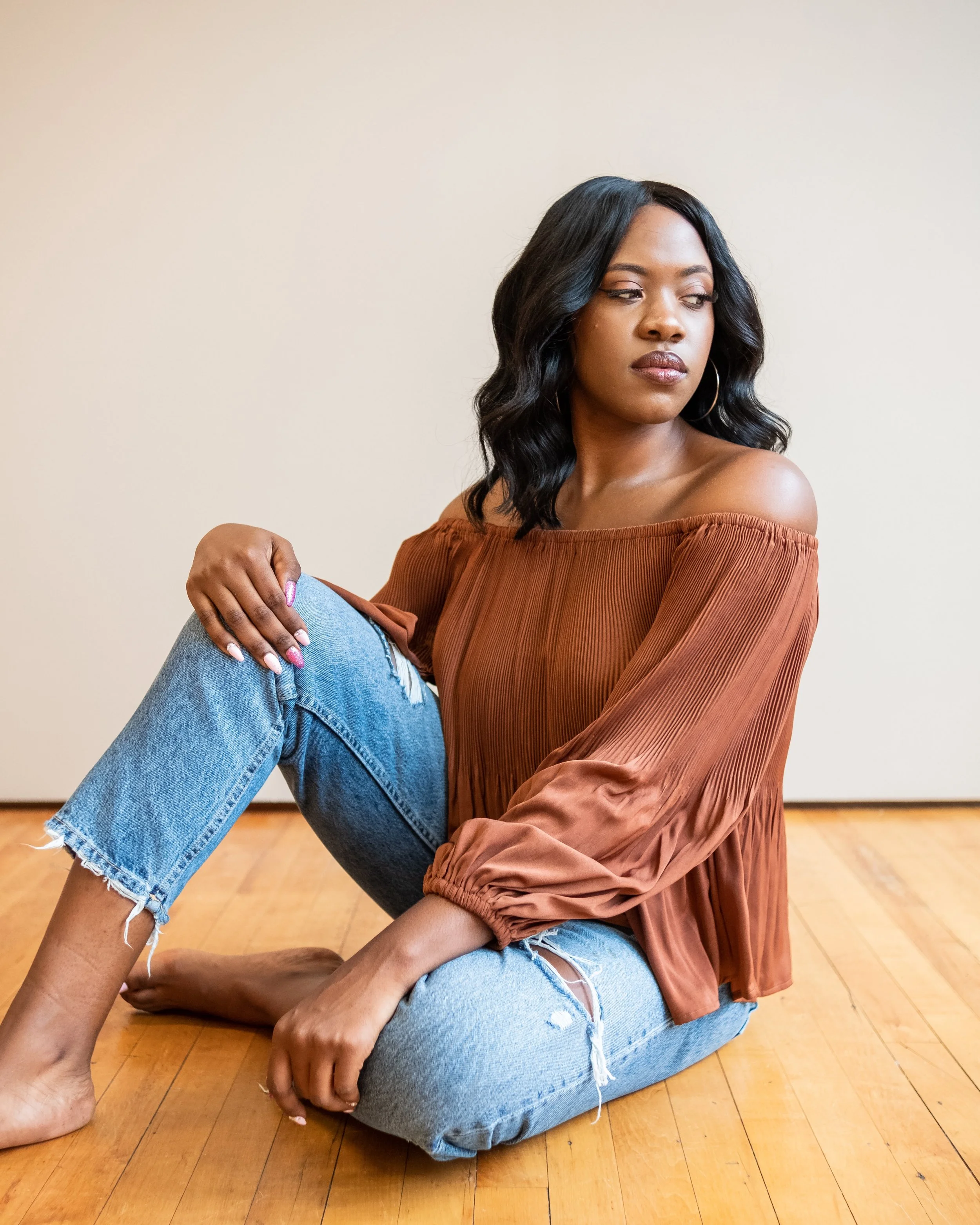Woman sitting on wooden floor in brown blouse and blue jeans