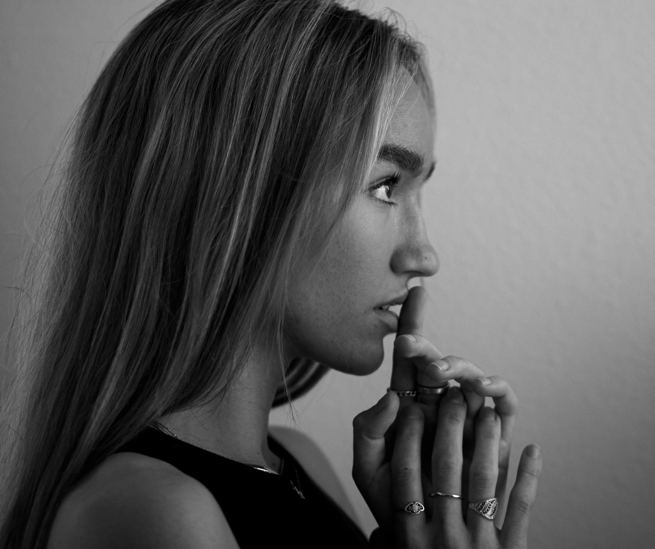 Black and white portrait of a woman in profile with long hair and several rings on her fingers, looking contemplative.