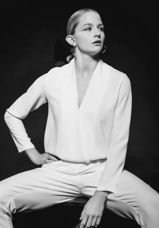 Black and white portrait of a person in a white suit sitting with a confident pose.