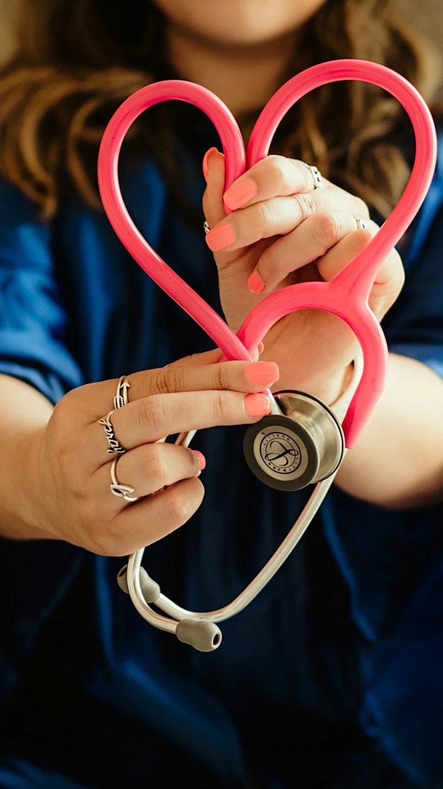 A woman holding a pink stethoscope in the shape of a heart.