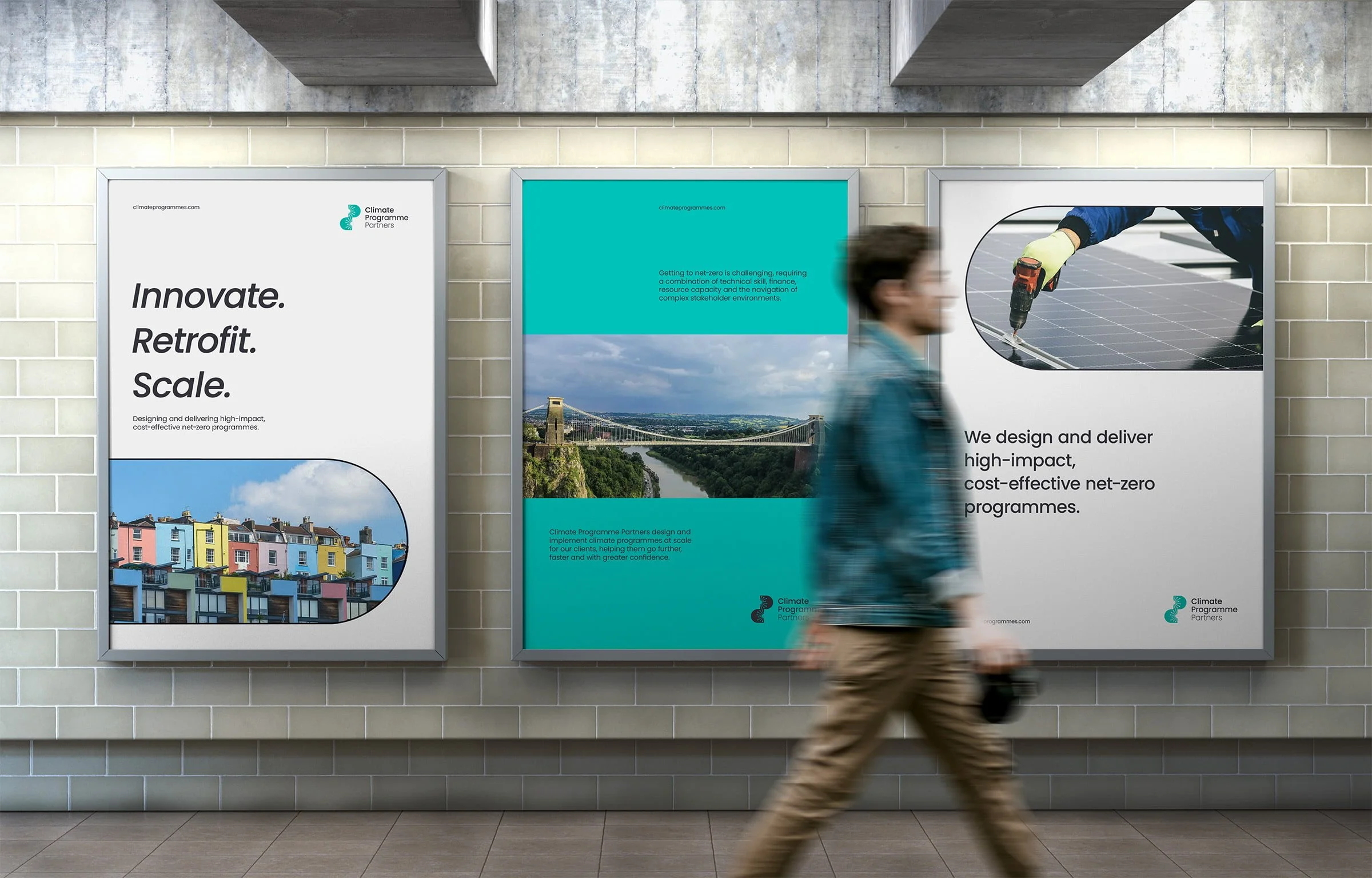 A person walking past three large posters on a subway or train station wall. The posters promote climate programs, featuring images of colorful houses, a bridge over a river, and solar panels being installed.