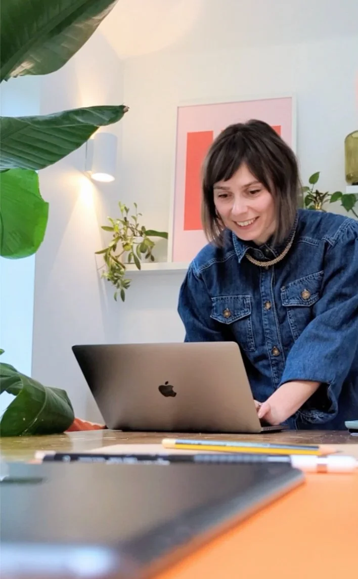 photo of tanya, website designer harringay, standing smiling and working from a laptop on a table