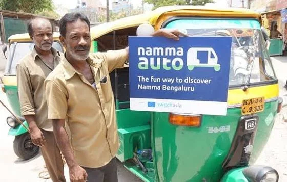 Two men standing beside a green auto-rickshaw holding a sign that reads 'Namma auto, The fun way to discover Namma Bengaluru'.