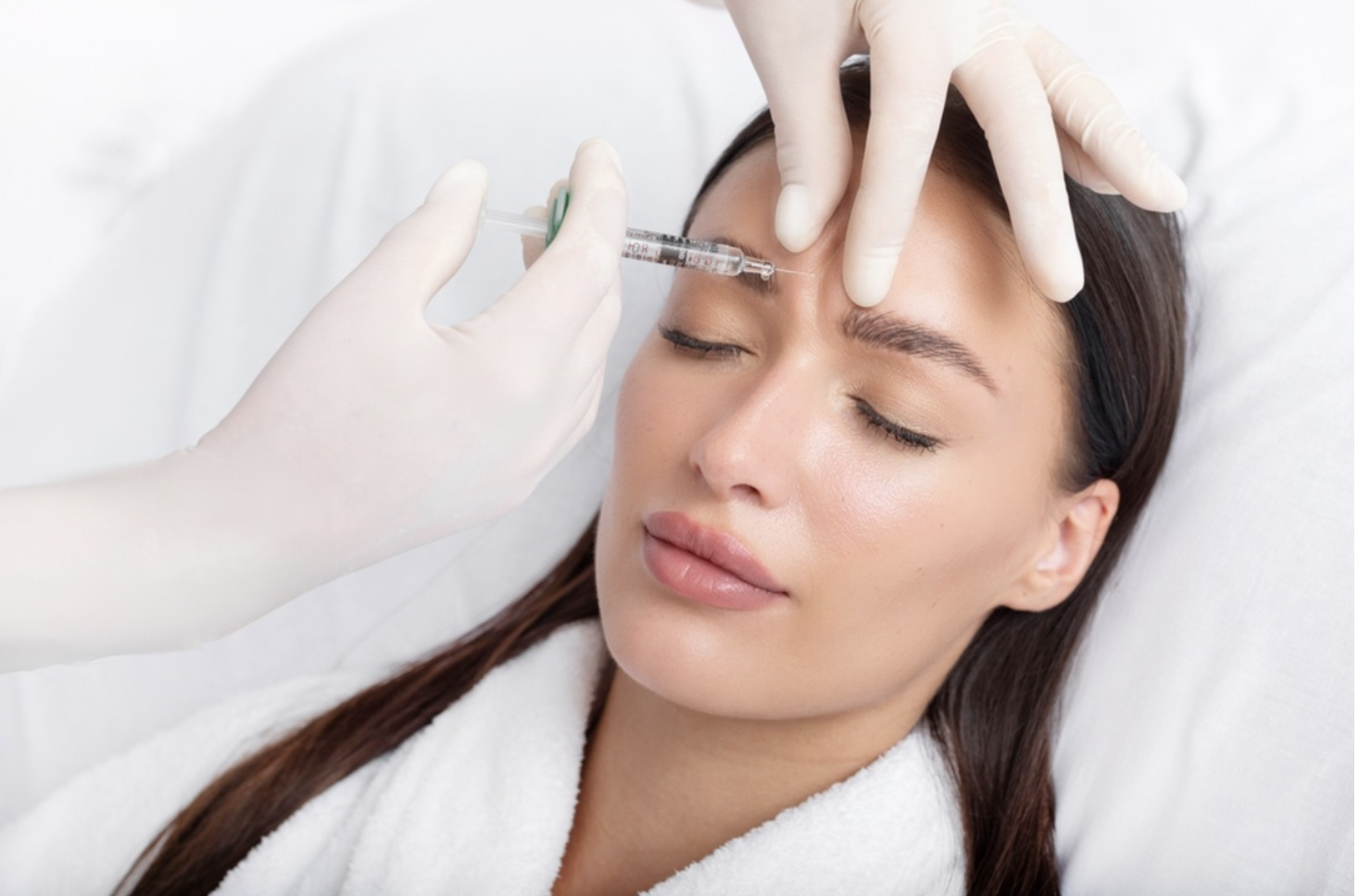 A woman receiving Botox injections on her forehead from a medical professional wearing white gloves.