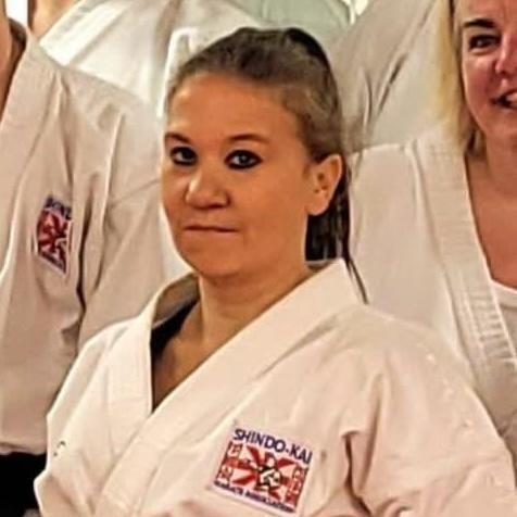 A woman in a karate uniform with a patch on her sleeve, standing among other martial artists.
