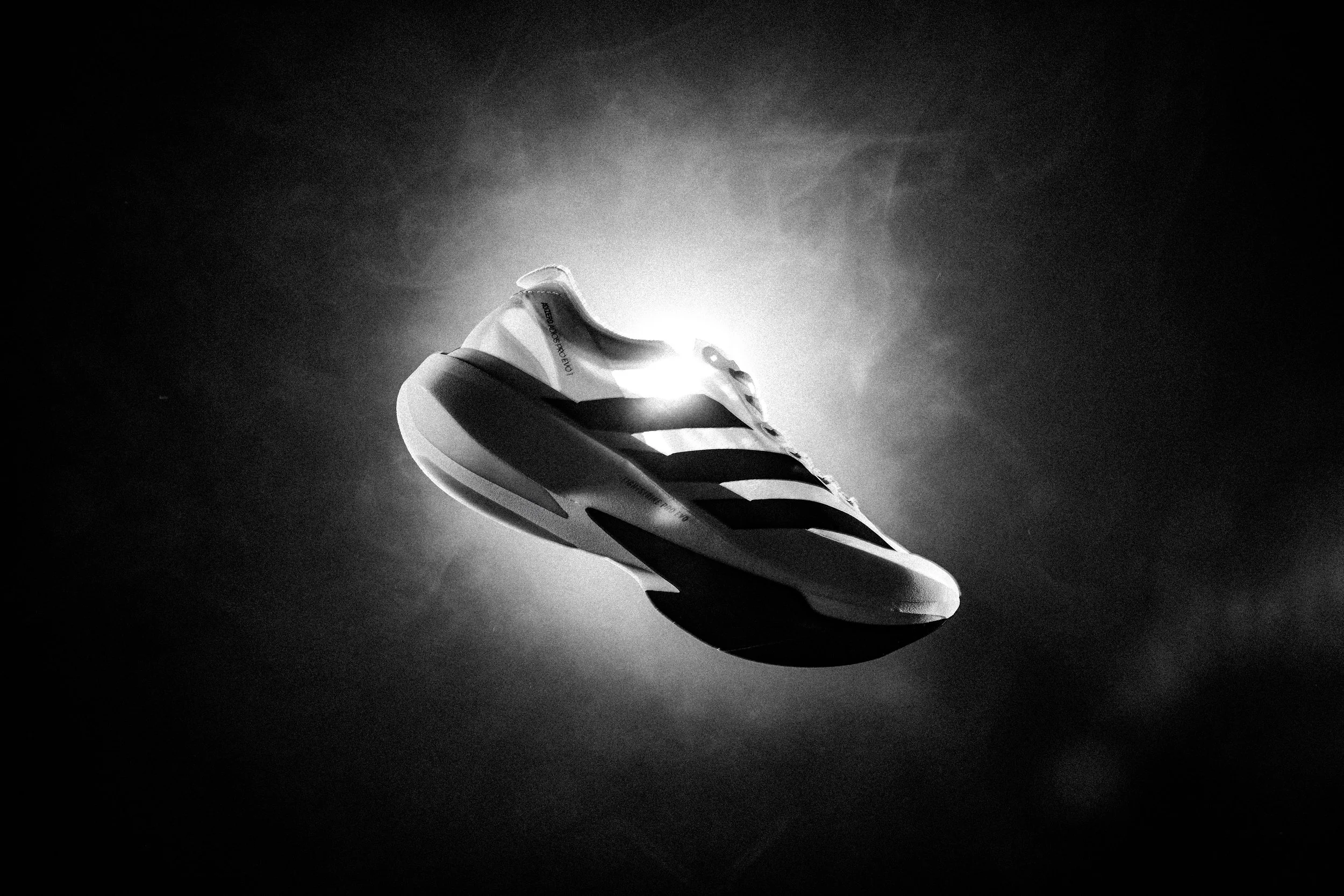 A running shoe floating in mid-air with a bright light source behind it, creating a glowing halo effect around the shoe in black and white.