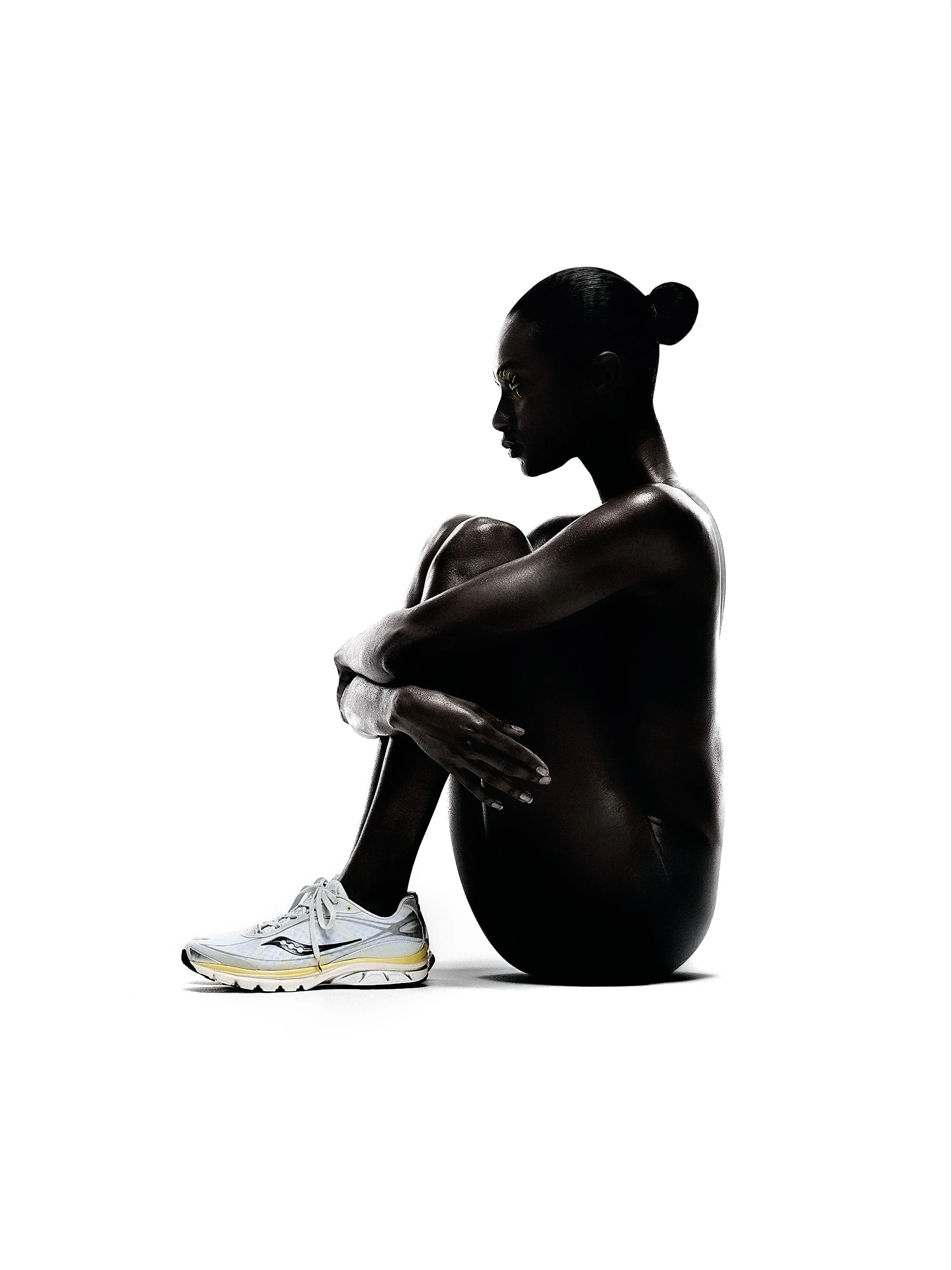 Silhouette of a woman sitting with her knees drawn up, wearing white sneakers, against a white background.