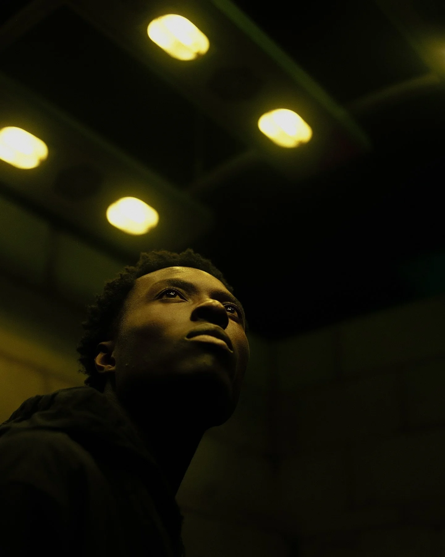 A young man looking up in a dimly lit room, with yellow ceiling lights overhead.