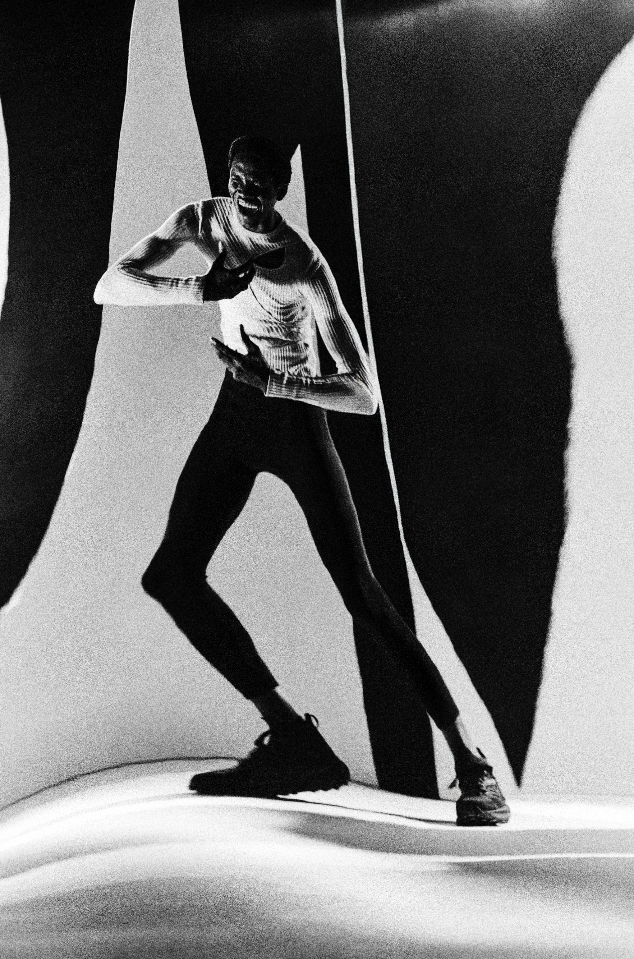 A black and white image of a person in running motion on a textured surface, with large abstract shapes in the background.