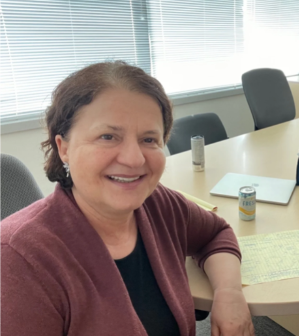 Two women smiling for a selfie in a conference room with a long light-colored table, chairs, and large windows with blinds in the background. Left side is Dr. Maria Hasenhuttl, a Principal Consultant, and Constance An, Managing Director of company. 