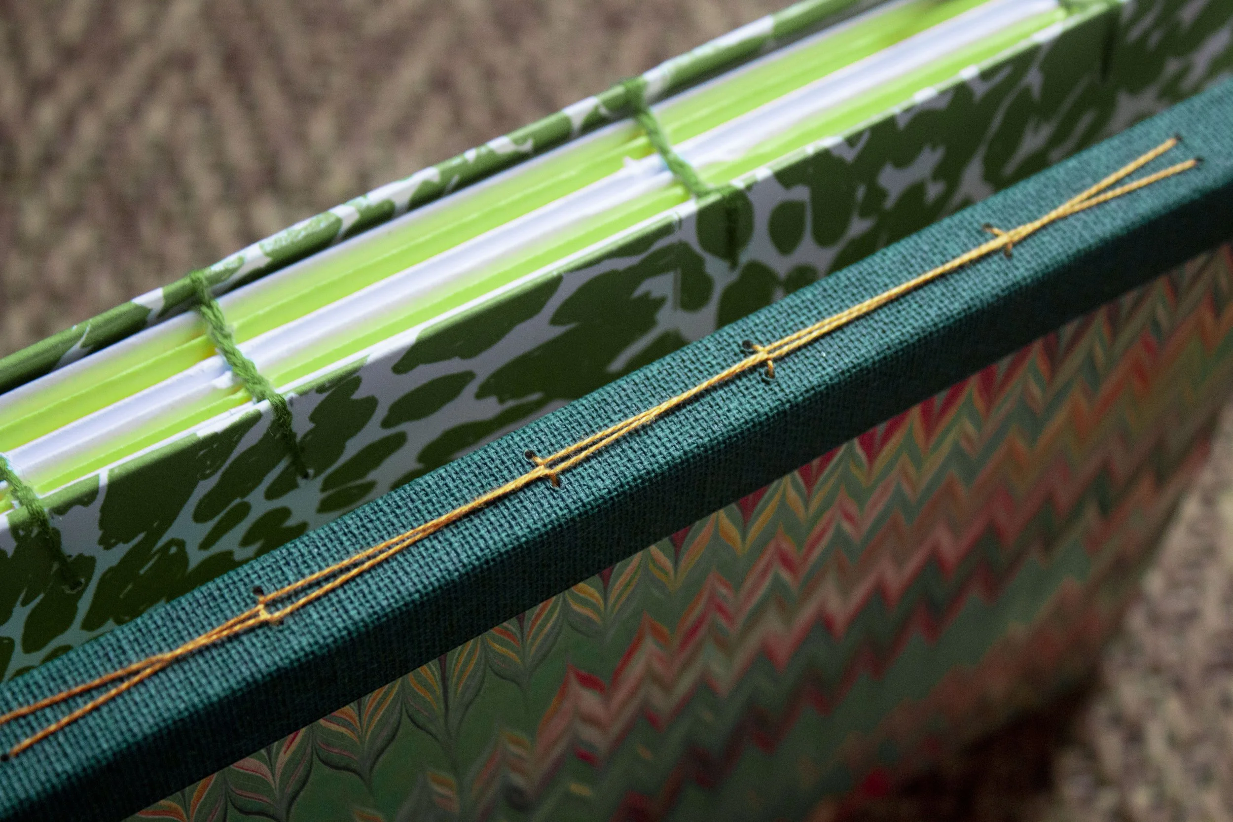 Premier plan d'un livre ou d'un cahier avec une couverture verte à motifs, coté supérieur un amas de livres ou de cahiers avec des pages blanches, reliés avec un ruban ou un fil de couleur jaune.