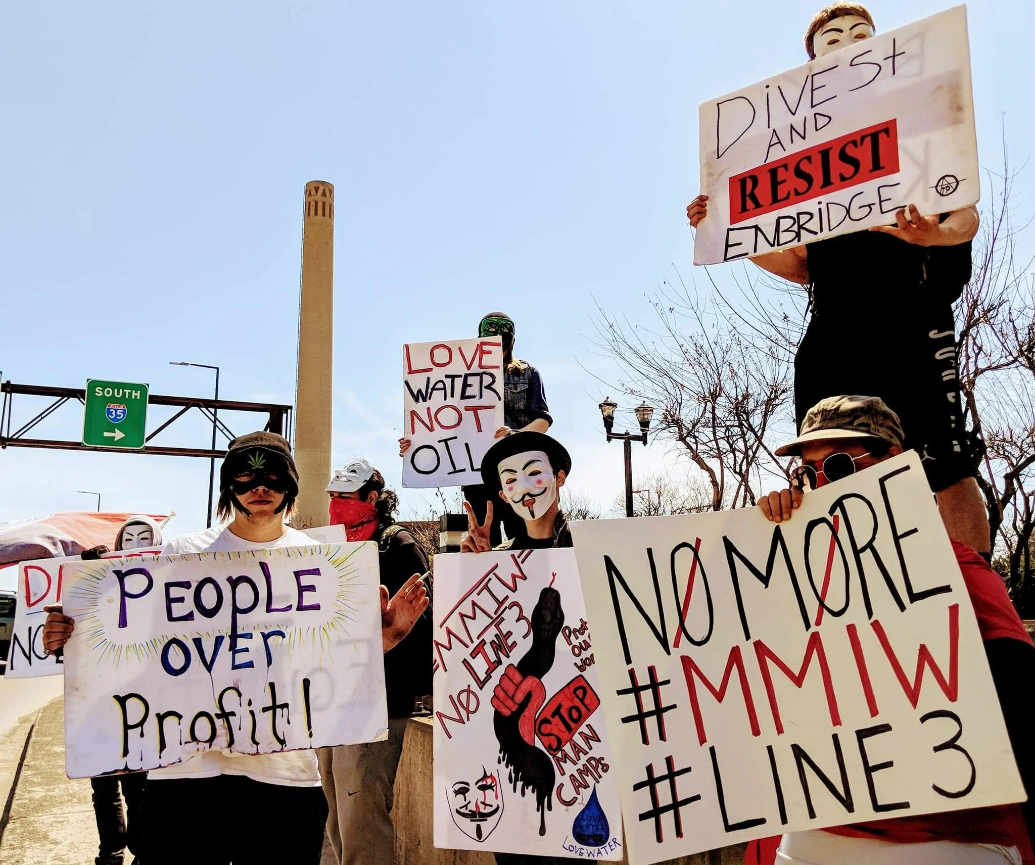 Members of the Anonymous group holds signs in protest of Line 3 Enbridge oil pipeline and to raise awareness of Missing and Murdered Indigenous Women
