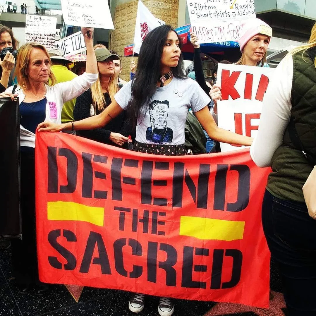 Young indigenous activist holds Defend the Sacred banner during Me Too rally in Los Angeles, California