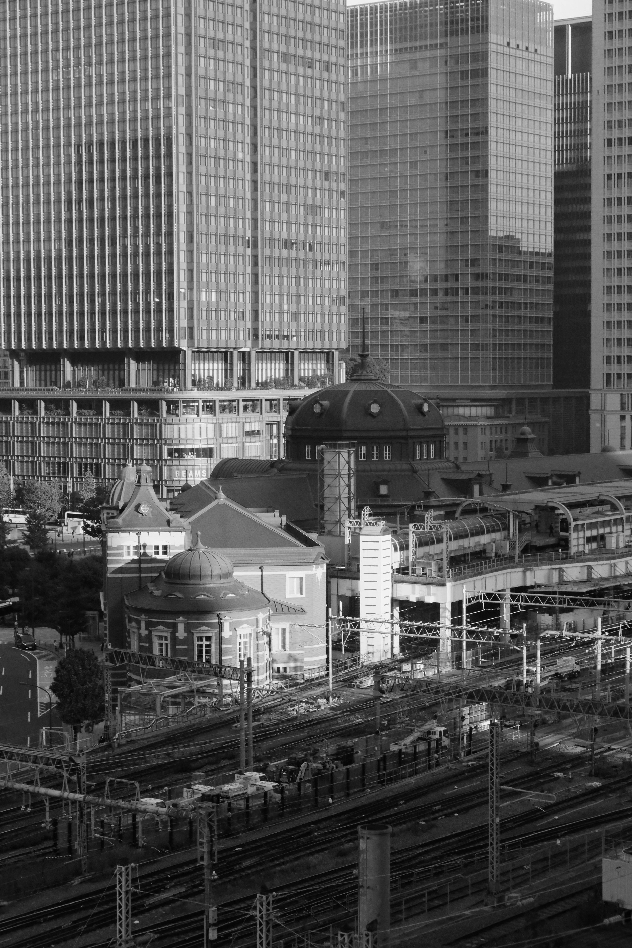 Black and white photo of a train station with historic architecture contrasting modern skyscrapers in the background.