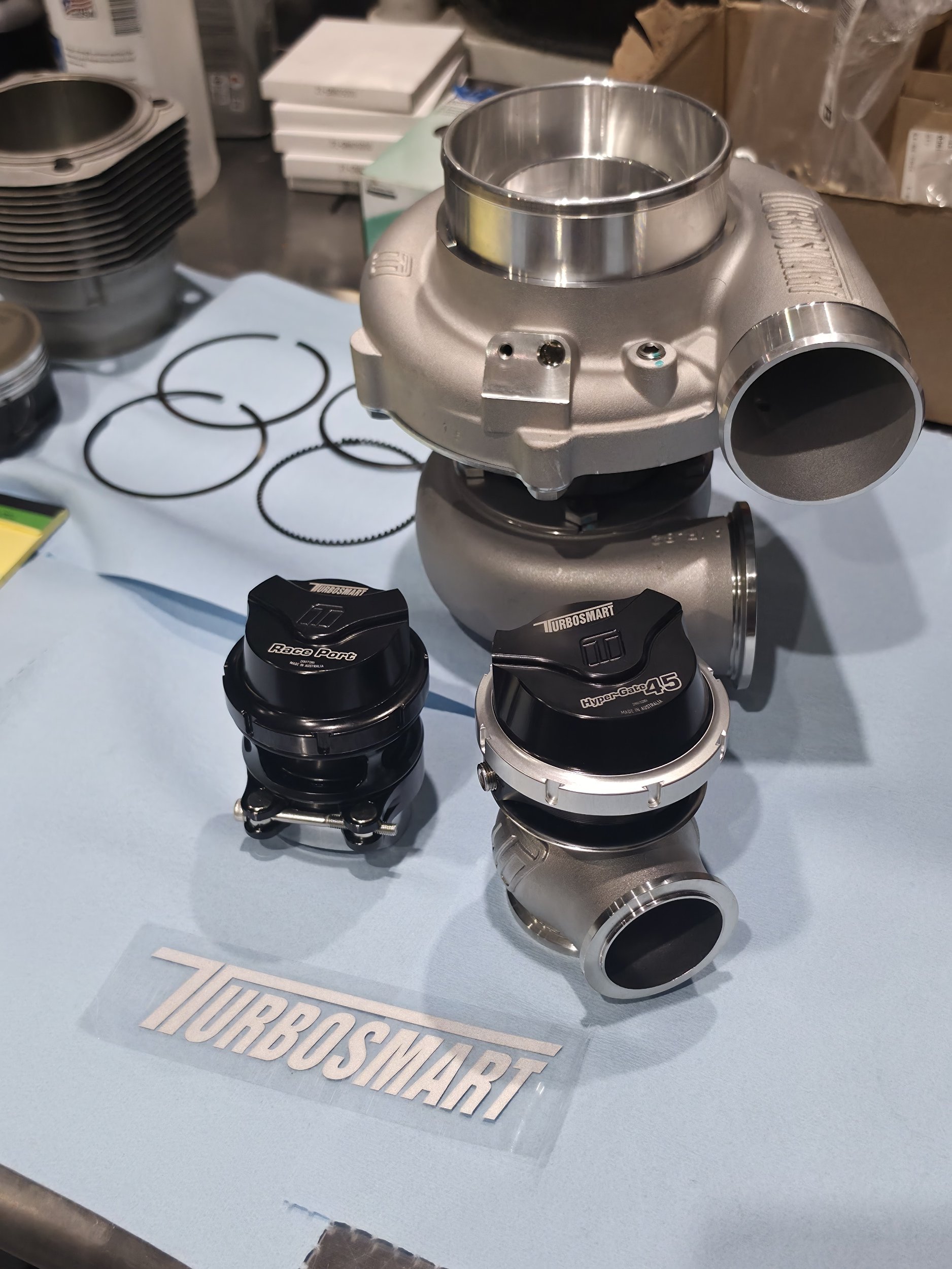 Turbosmart automotive turbocharger and wastegate components, including RacePort and Hyper-Gate 45 models, displayed on a workbench.
