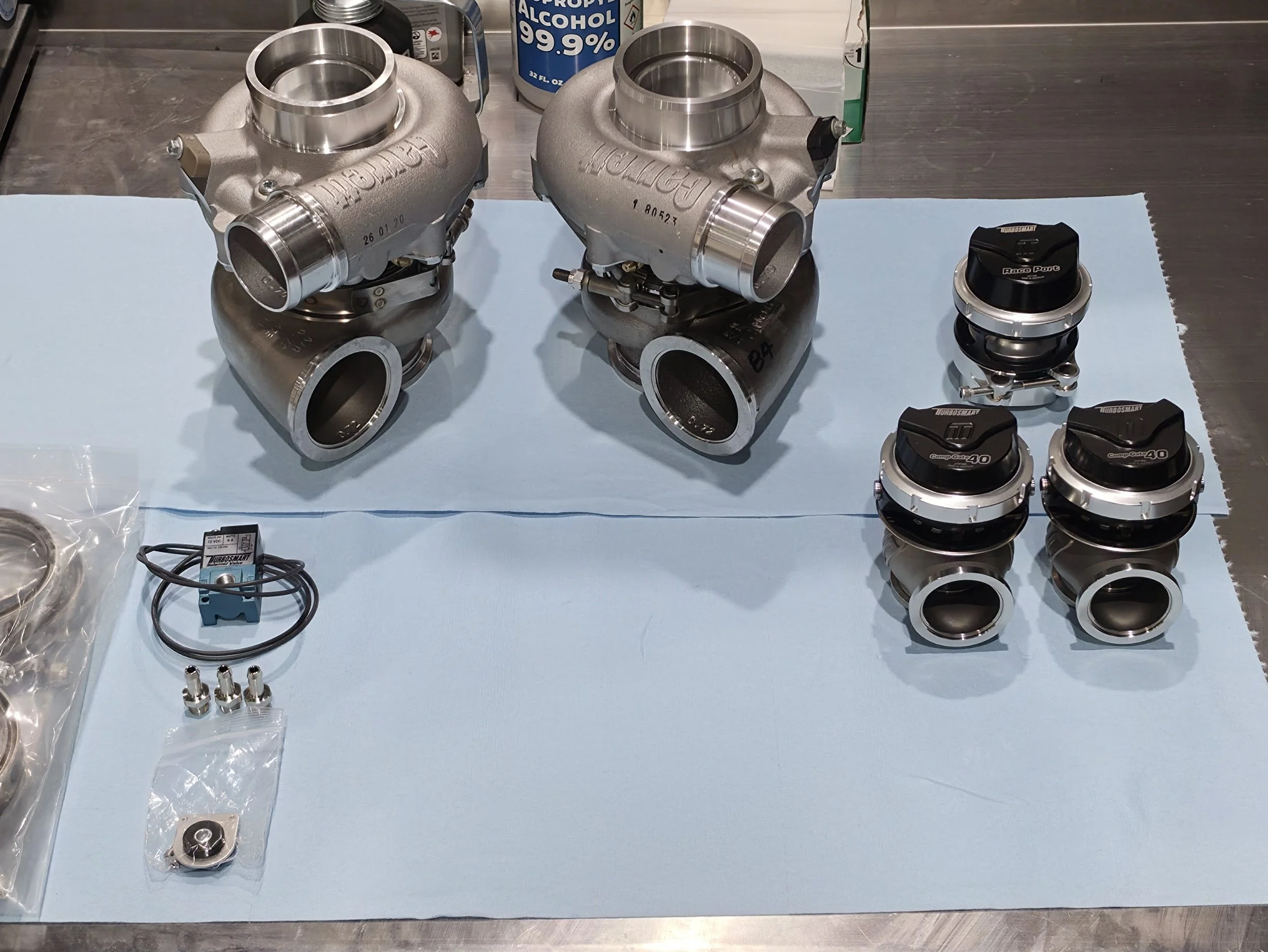 Two Turbosmart turbochargers with Comp-Gate40 and Race Port wastegates, fittings, seals, and installation hardware arranged on a workbench.