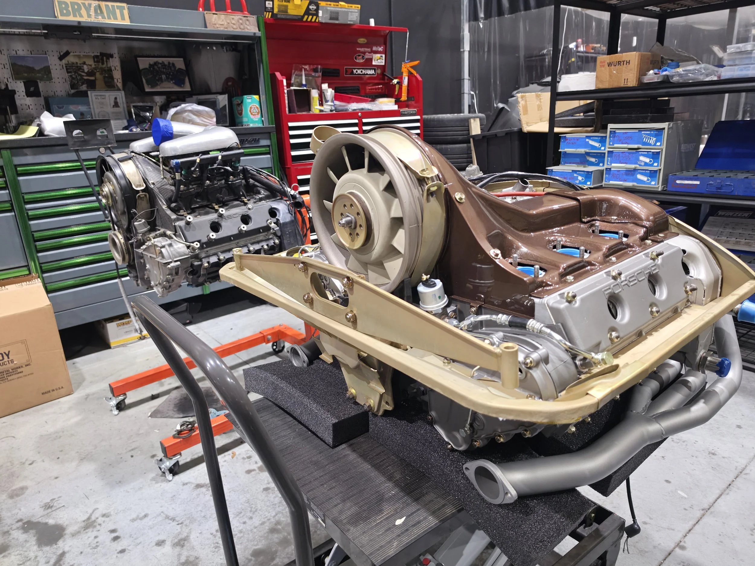 Porsche engine and transmission assembly on a workshop stand surrounded by automotive tools and parts