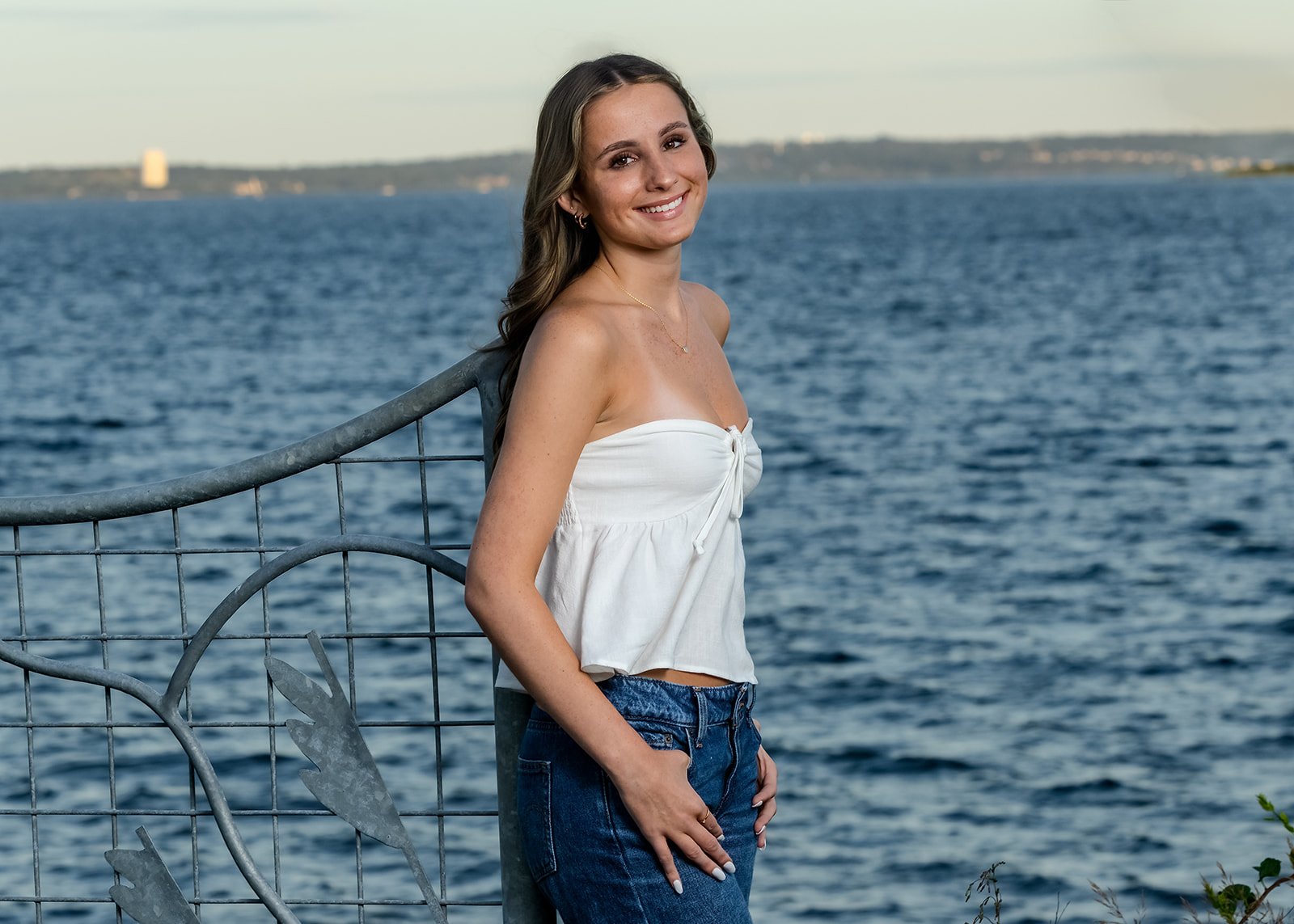 High school senior girl in a white top and jeans with Narragansett Bay in the background at Rocky Point State Park in Warwick, Rhode Island.