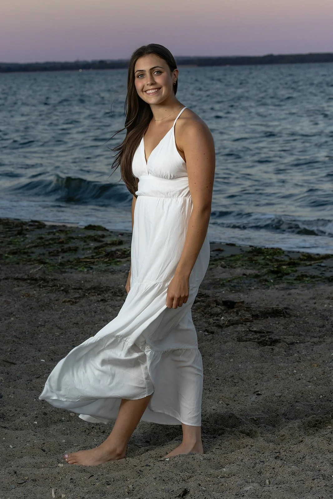 High school senior girl in a white dress at sunset on the beach at Rocky Point State Park in Warwick, Rhode Island.