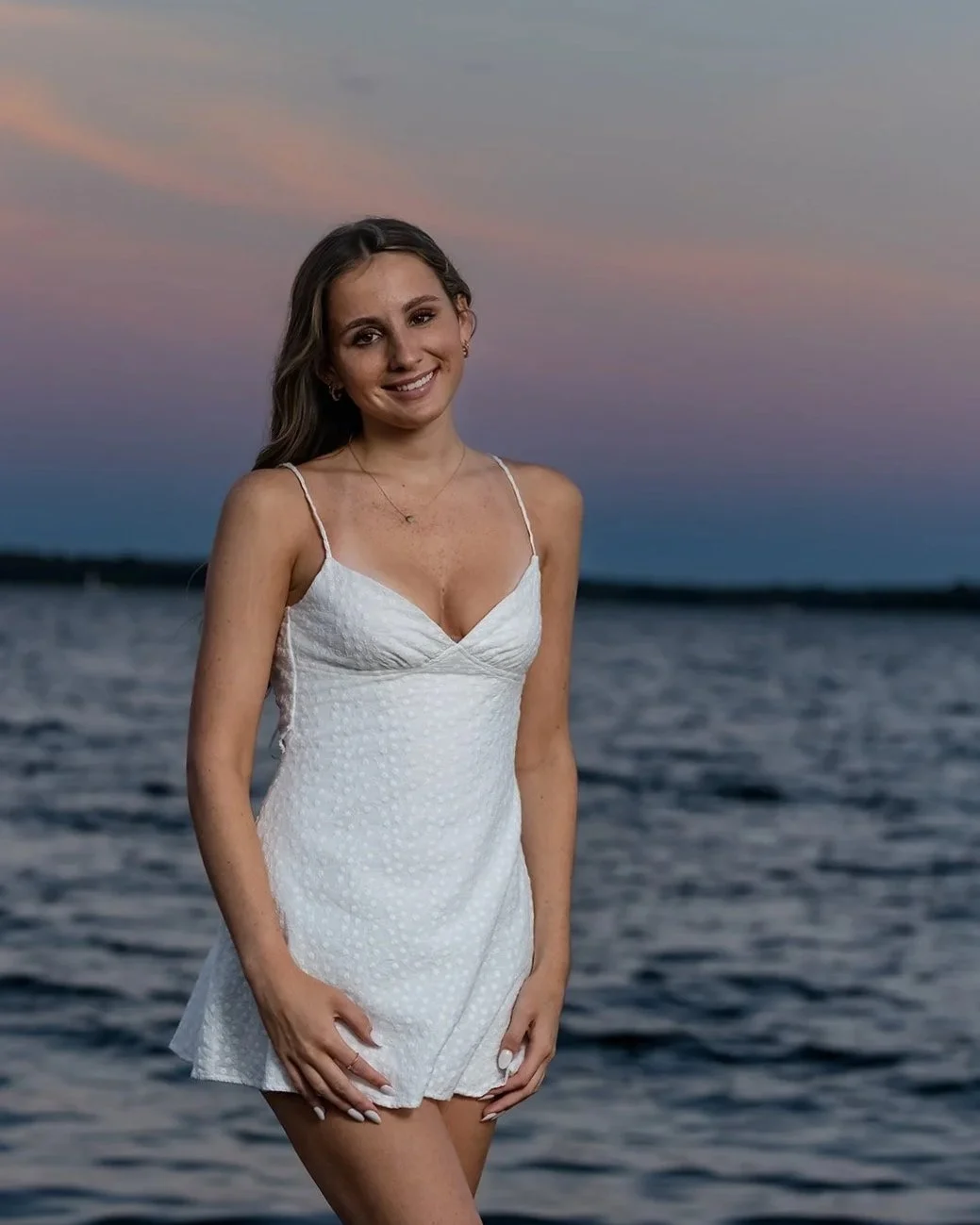 High school senior girl in a white dress with a cotton candy sky sunset at Rocky Point State Park in Warwick, Rhode Island.