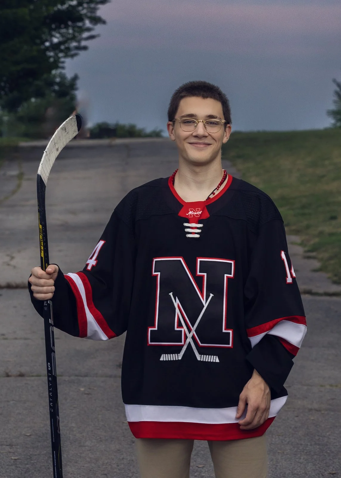 High school senior boy in his hockey jersey holding his hockey stick at Rocky Point State Park in Warwick, Rhode Island.