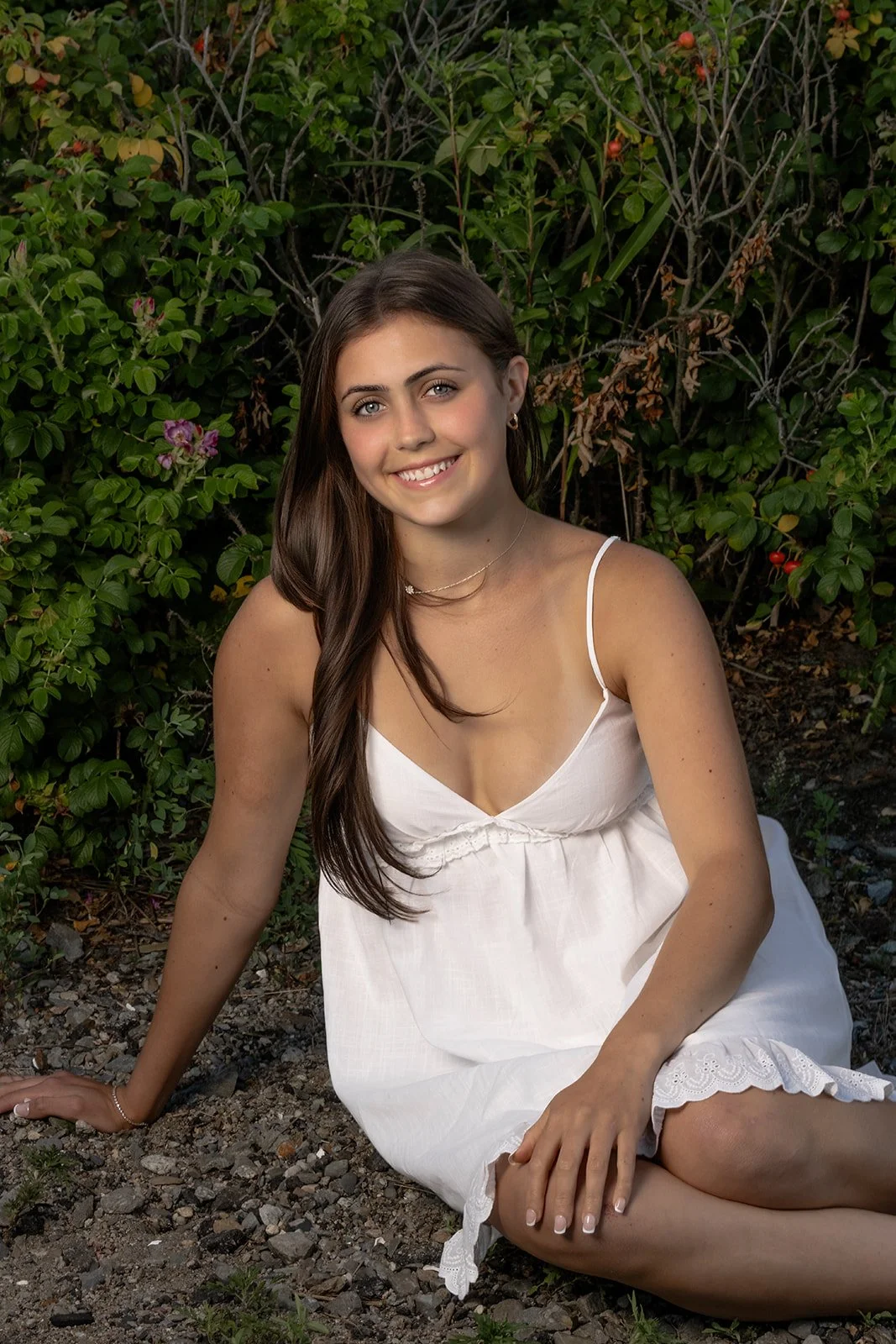 High School senior in a white dress posing near coastal greenery at Rocky Point State Park in Warwick, Rhode Island.