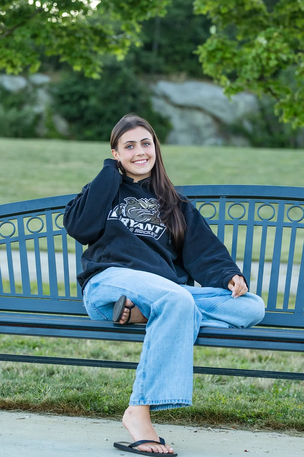 High School senior in her college sweatshirt posing on a park bench at Rocky Point State Park in Warwick, Rhode Island.
