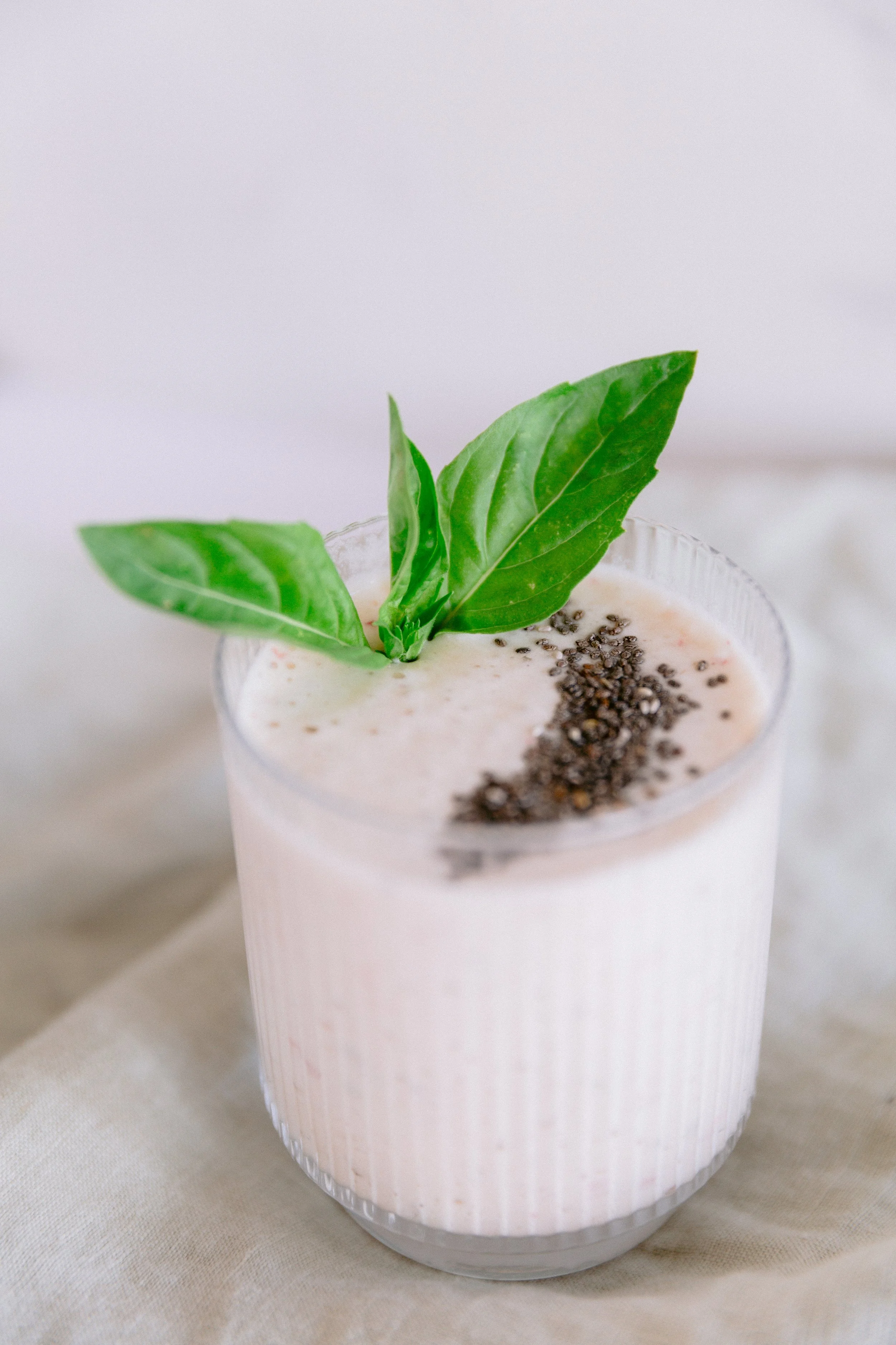 A creamy pink cocktail garnished with basil leaves and black pepper in a clear glass.