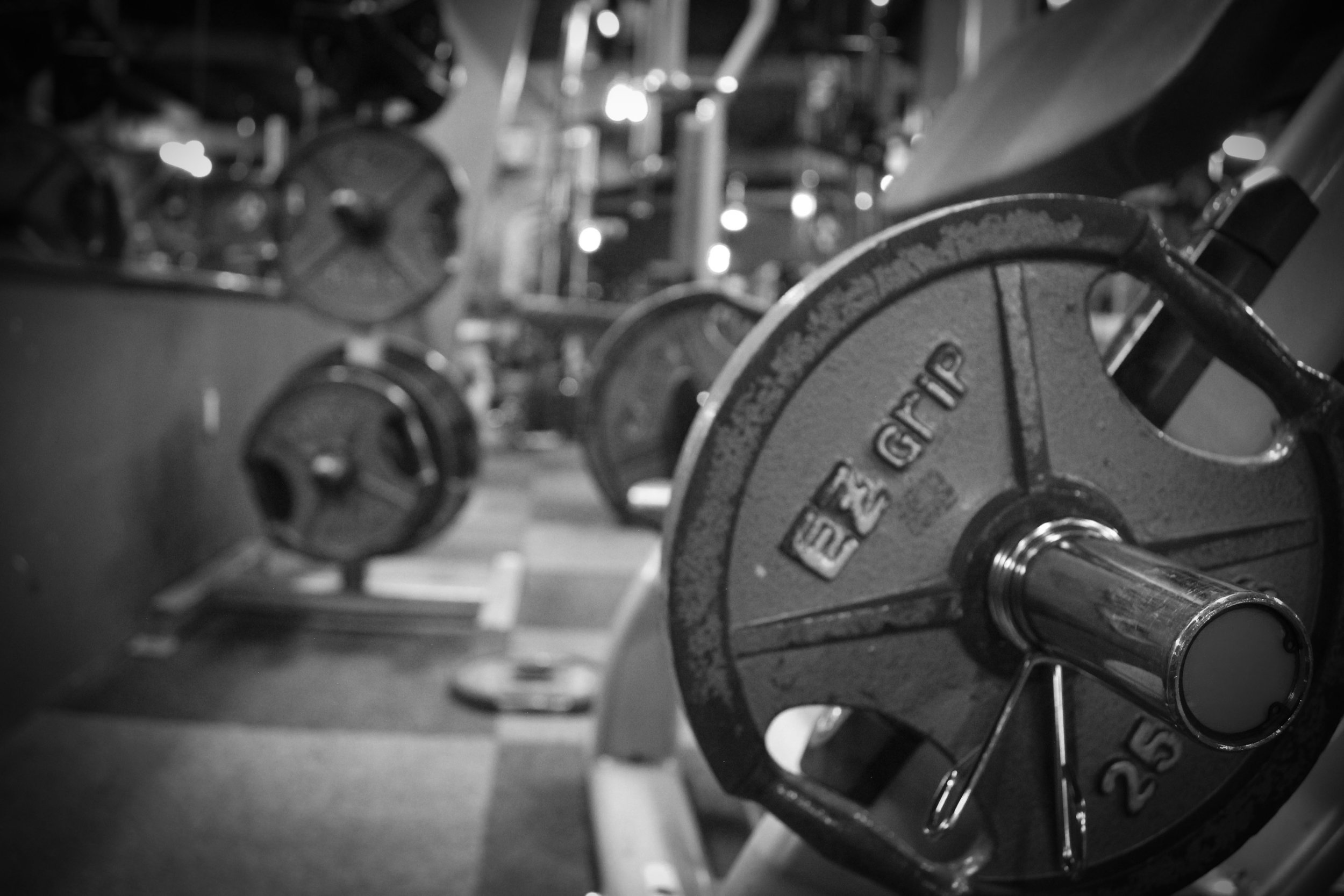 Black-and-white close-up of a 25-pound EZ Grip weight plate loaded onto a barbell in a gym setting.