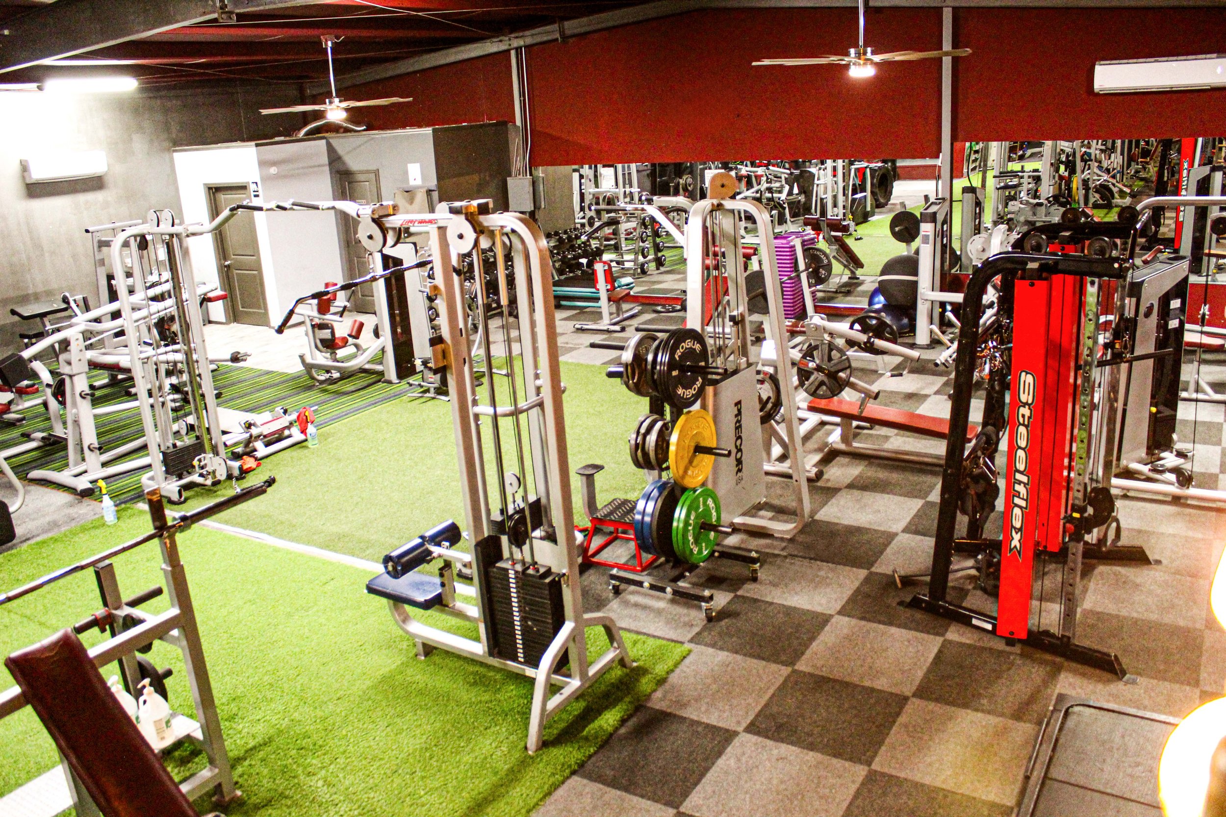 Overhead view of a gym featuring a mix of strength training machines, free weights with colorful plates, and functional training areas on turf and checkered flooring