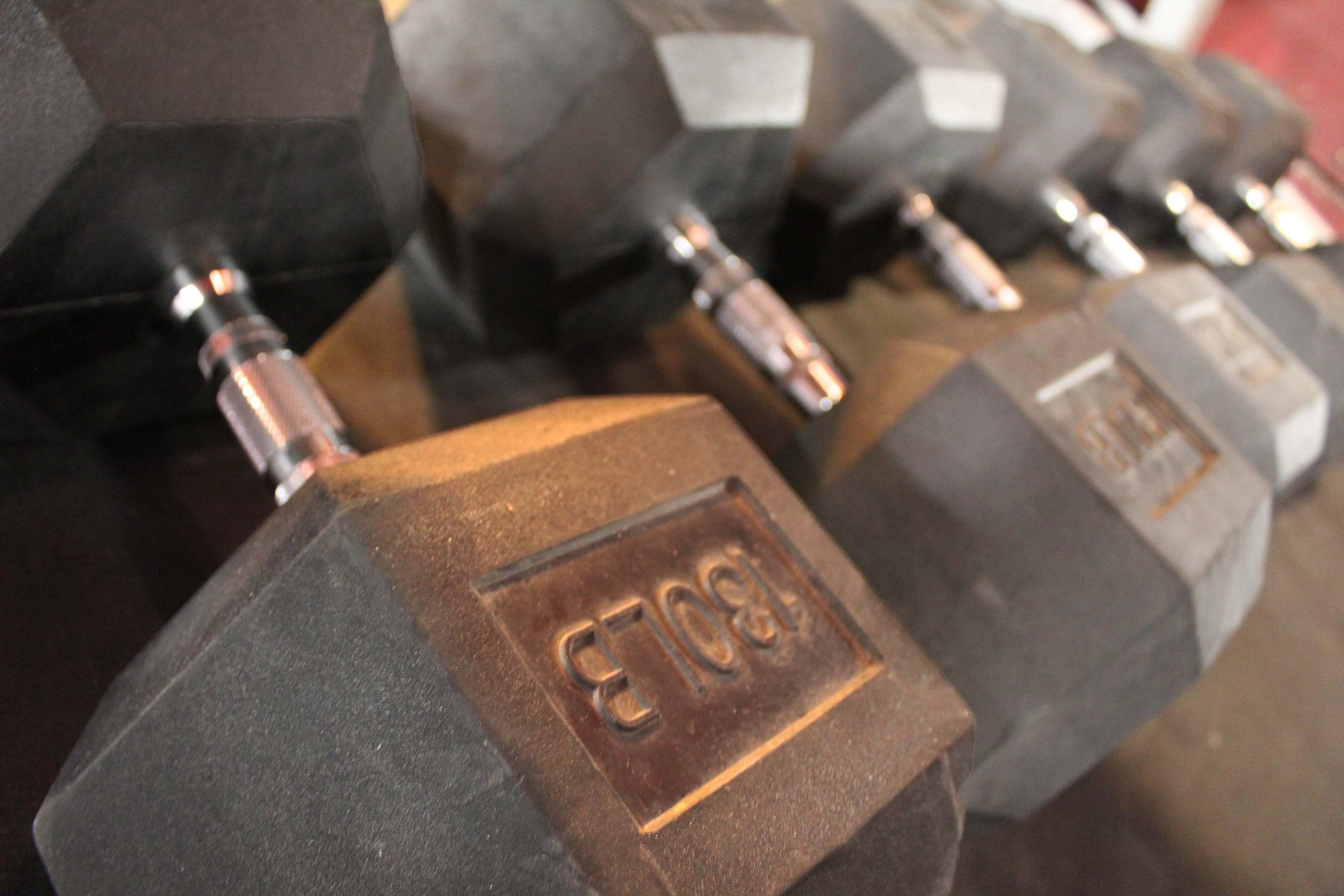 Close-up of heavy 130 pound black hexagonal dumbbells with chrome handles, arranged in a row on a gym floor.