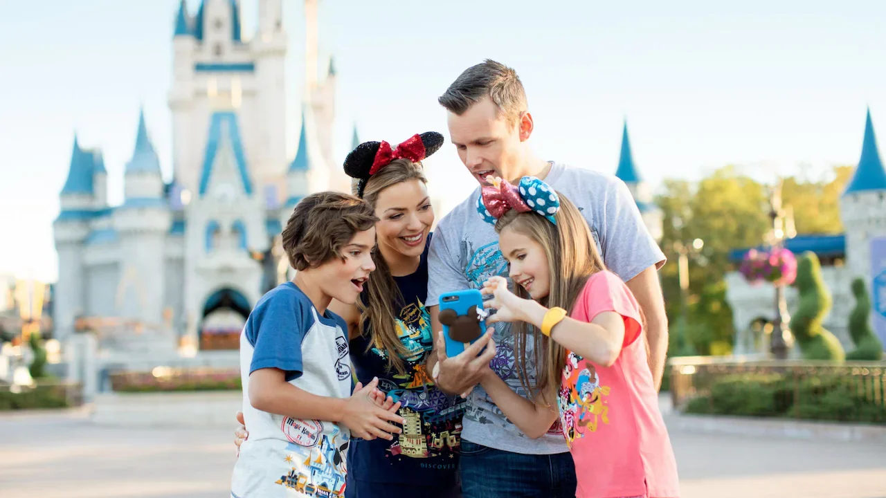 Family of four looking at a phone, with a castle in the background at a Disney theme park, all wearing Minnie Mouse ears.